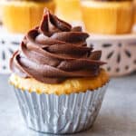 chocolate fudge frosting piped onto a yellow cupcake in a silver liner.