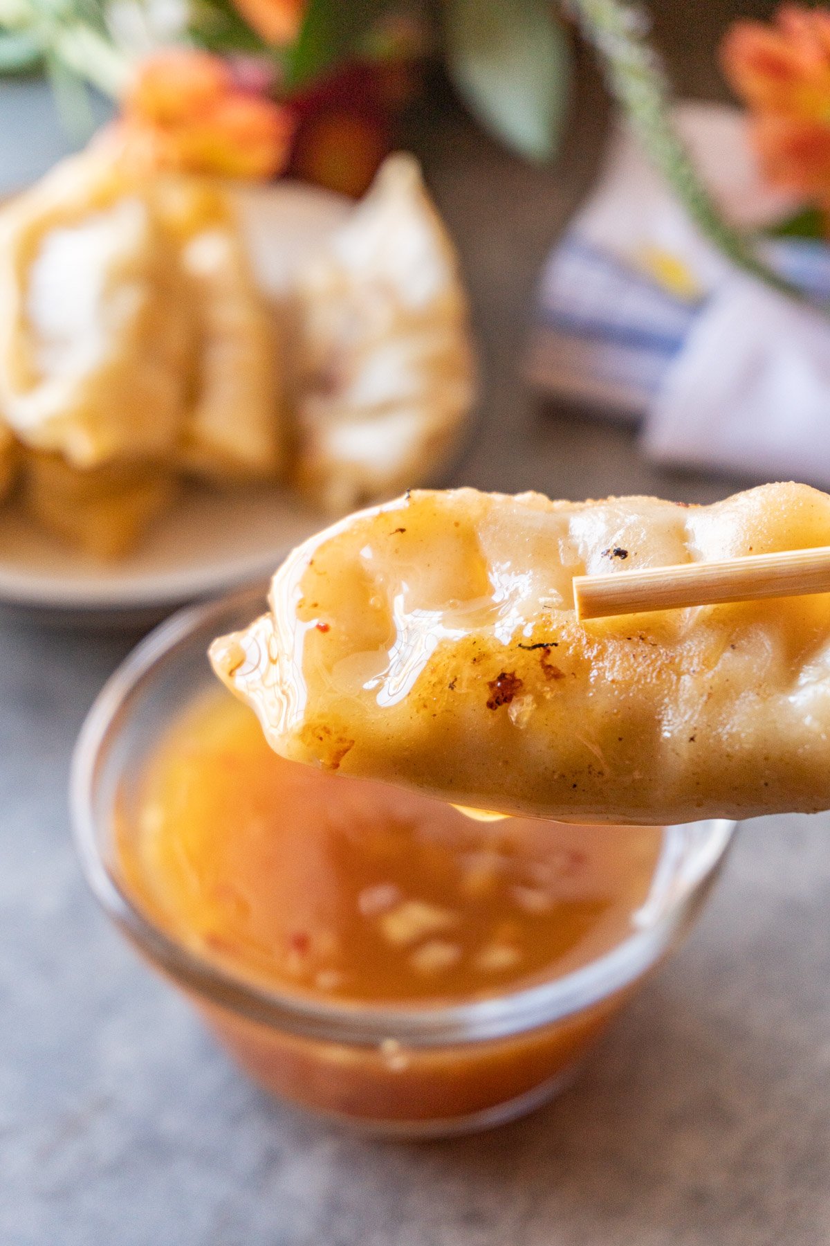 potsticker held in chopsticks with sauce on top.