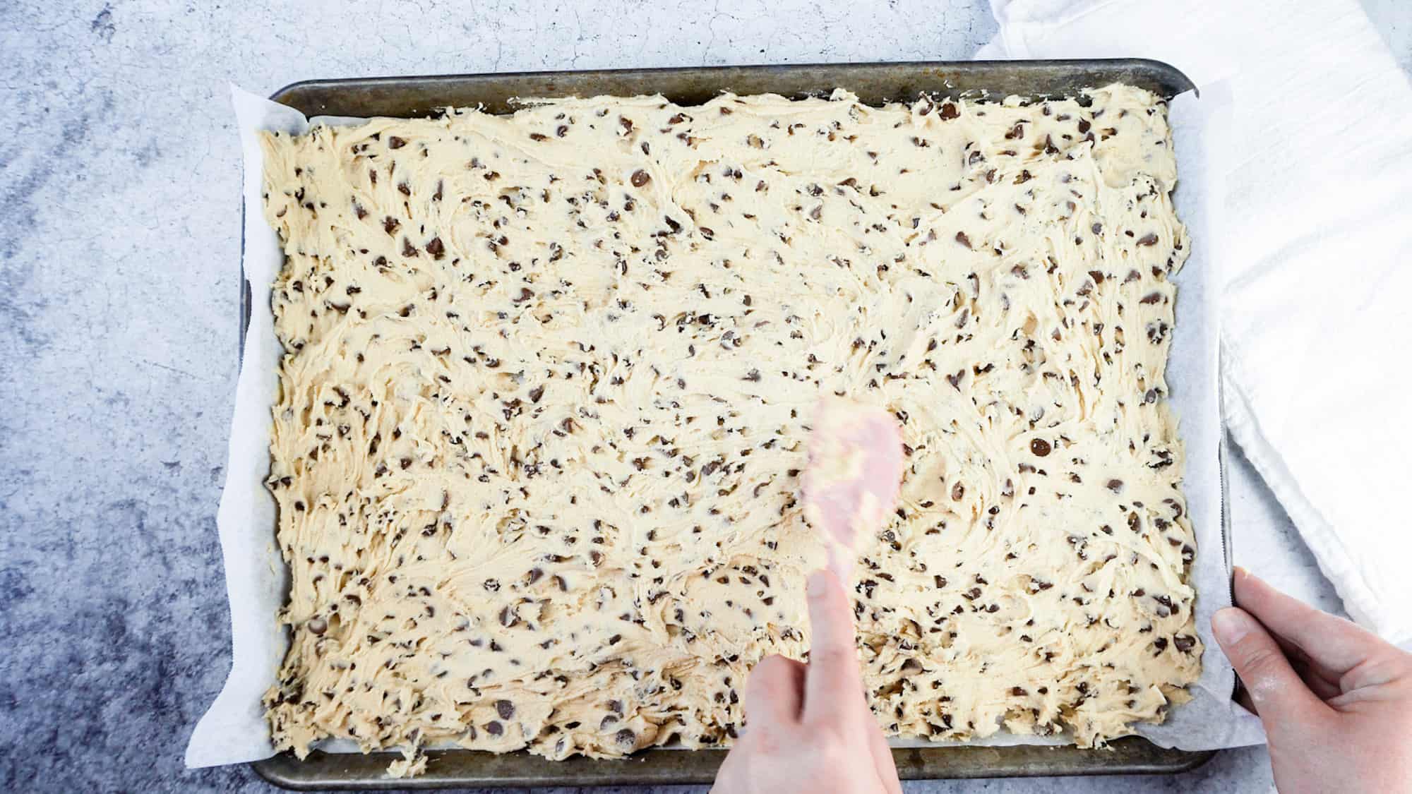 chocolate chip cookie bar dough spread out in sheet pan