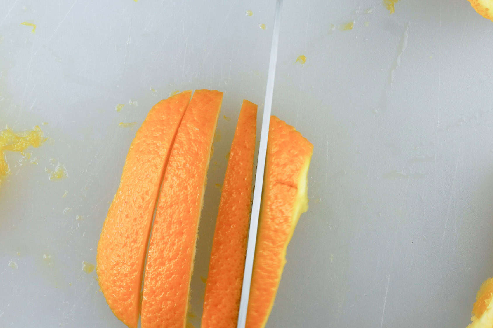 cutting an orange peel into slices on a cutting board.