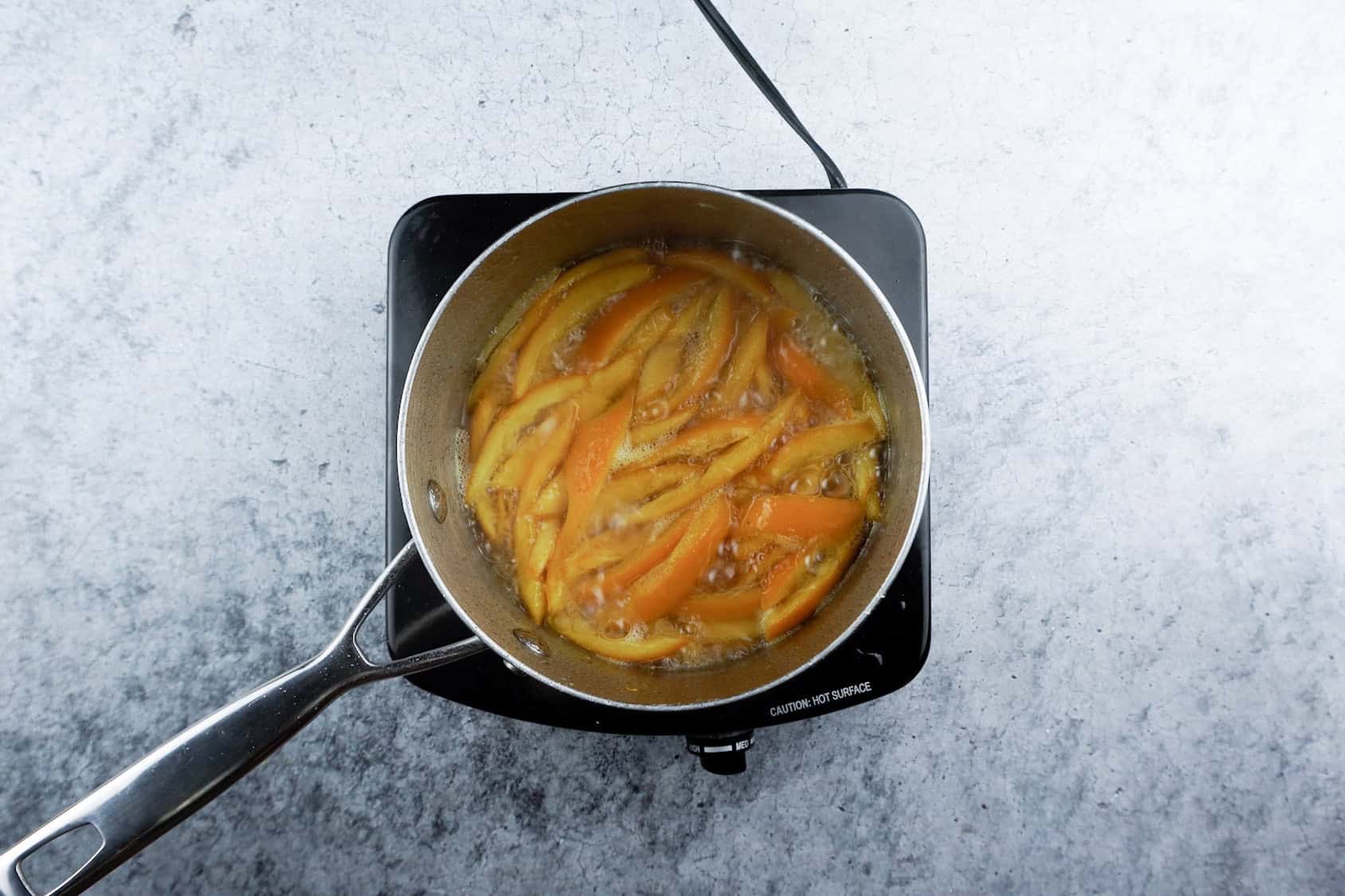 boiling orange peels in sugar water in a saucepan.