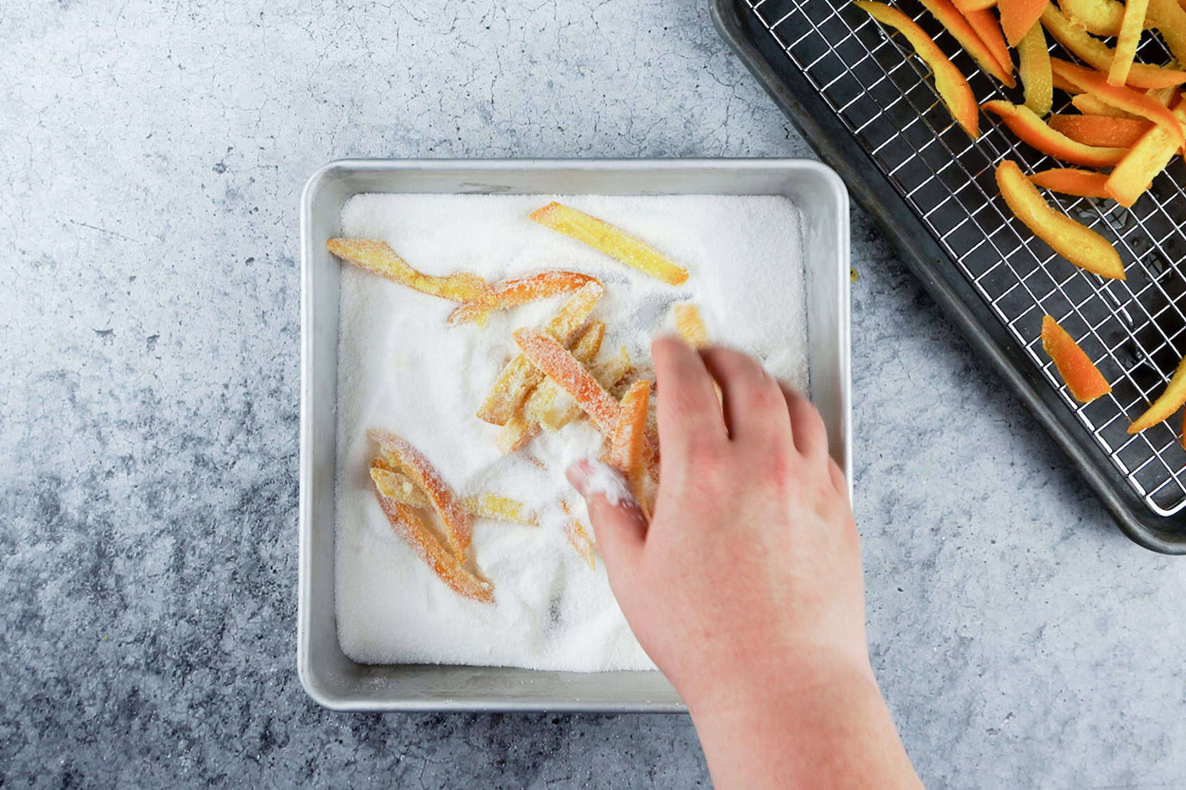 coating candied orange peels in sugar in a square dish.