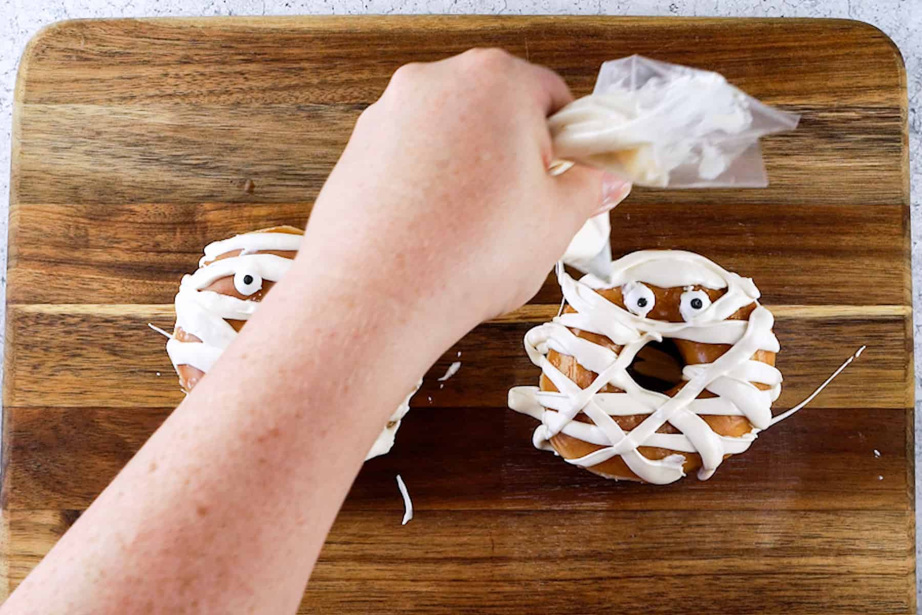 piping on mummy wrappings to mummy donuts using white candy melts in a piping bag..