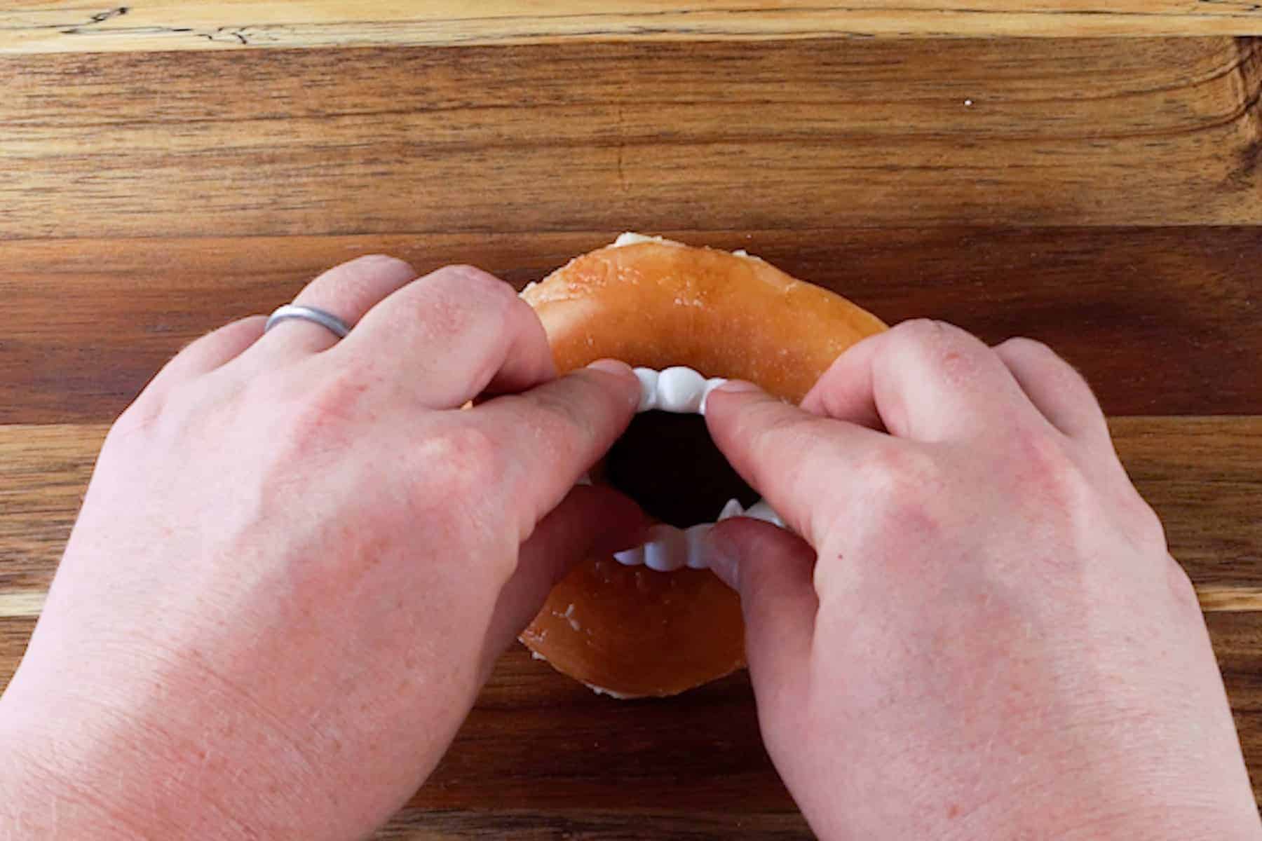 adding plastic vampire fang teeth to a glazed donut.