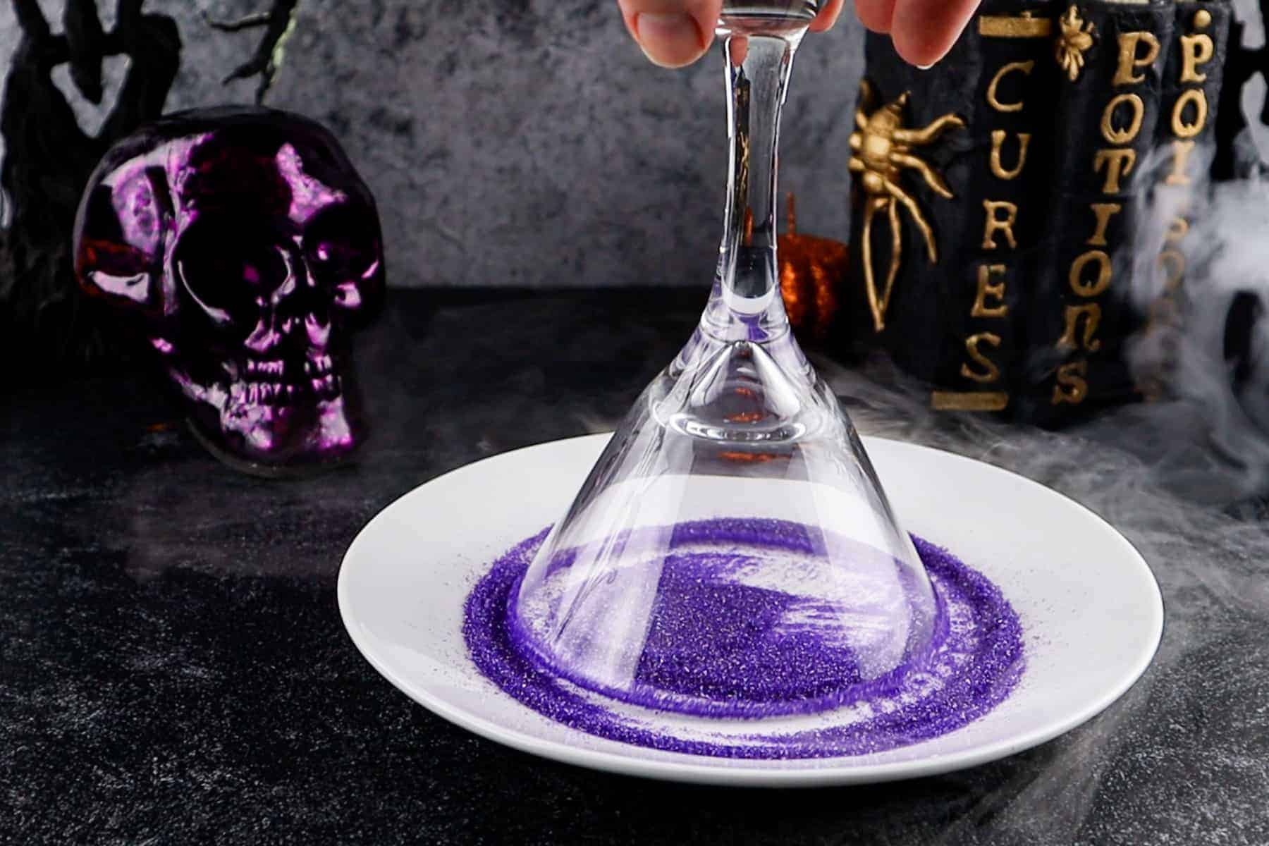 dipping the rim of a glass into purple sanding surgar sprinkles