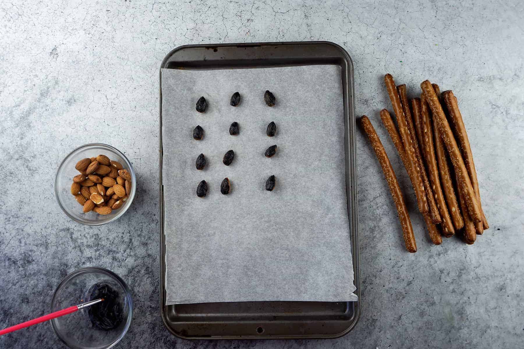 almonds painted with black frosting on parchment-lined baking sheet.