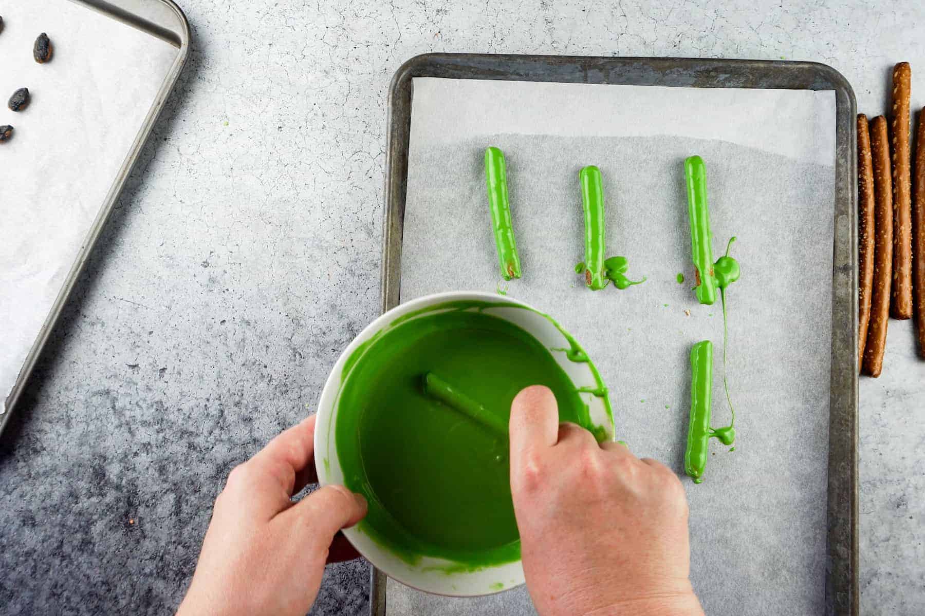 coating a pretzel rod in green candy melts.