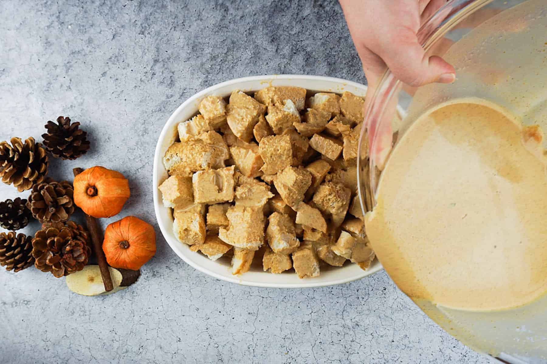 Pouring the filling over the cubed bread in the white dish.