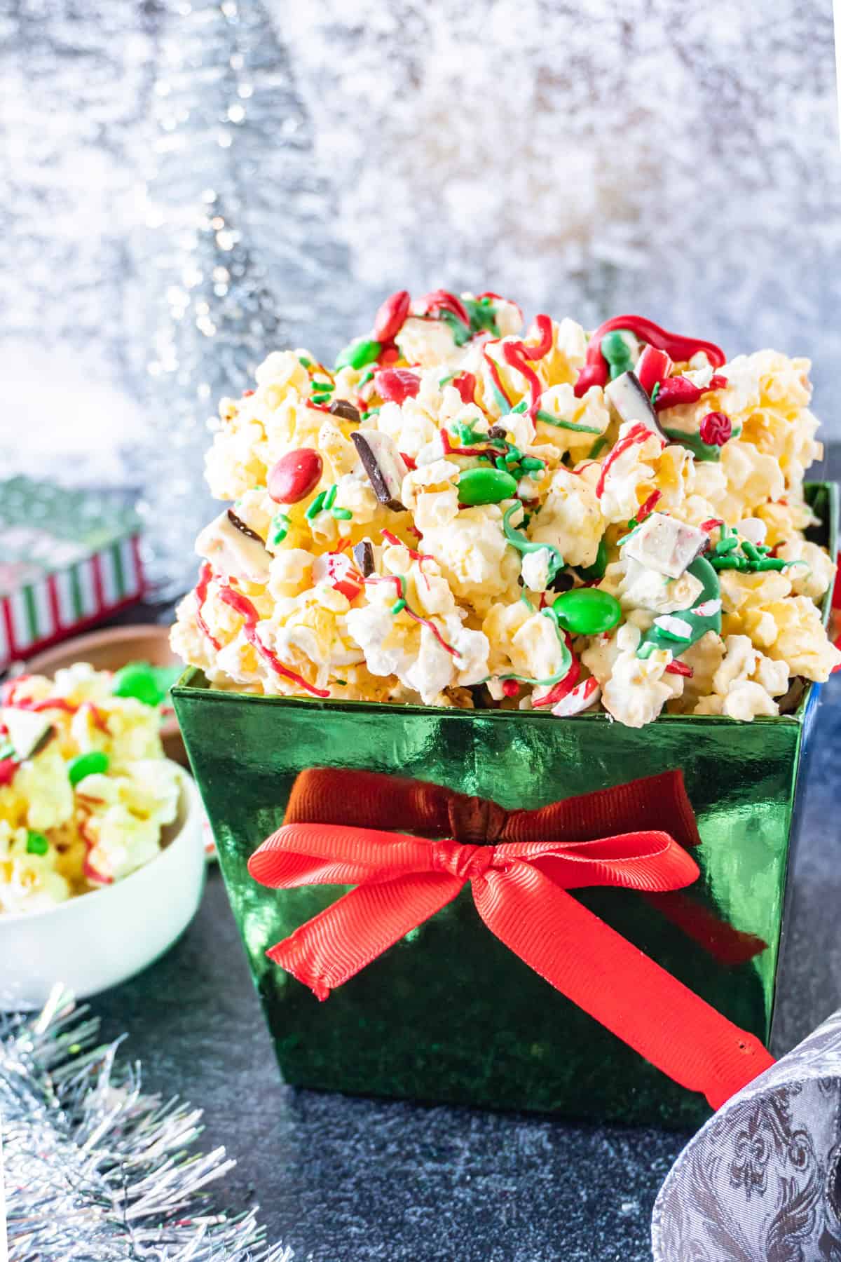 Christmas popcorn in a shiny green box with a red bow, with Christmas decorations in the background.