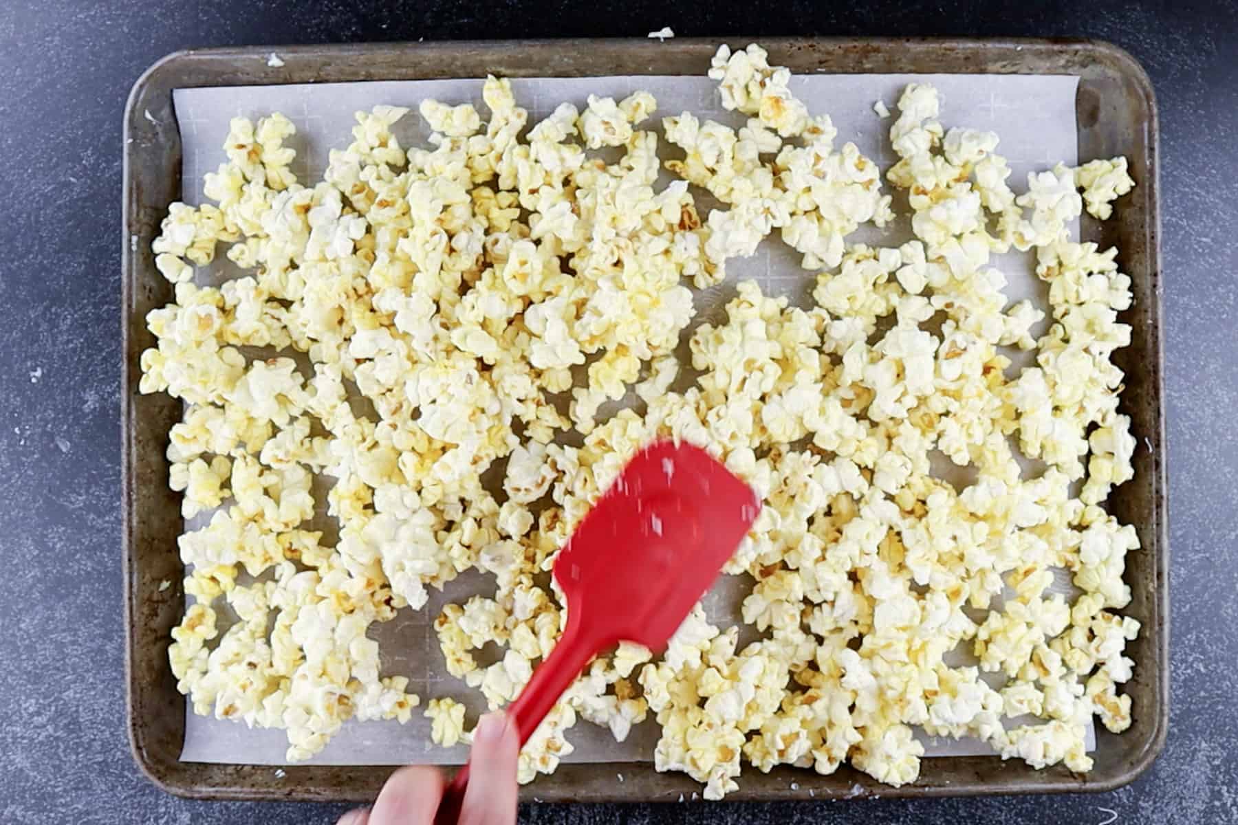 spreading white chocolate covered popcorn on baking sheet.