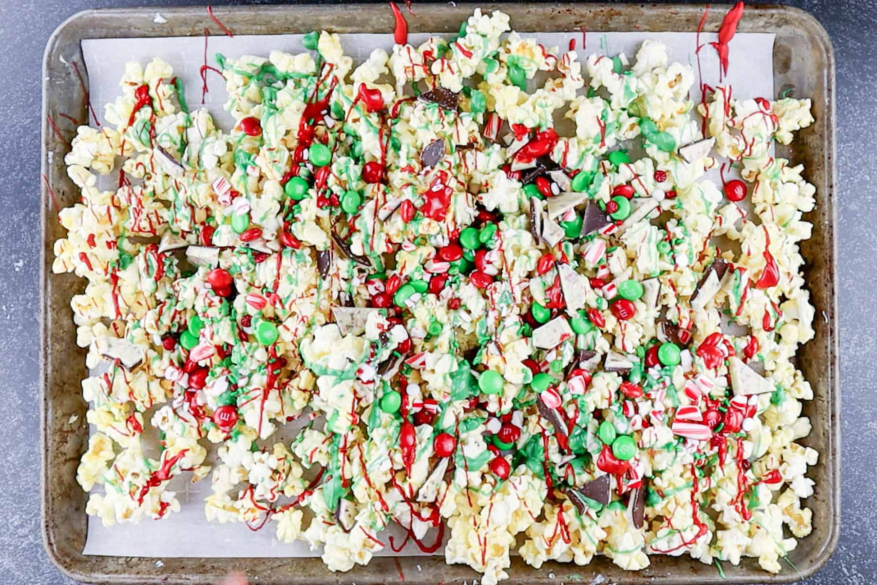 Popcorn drizzled with candy melts and sprinkled with candy and sprinkles on baking sheet.