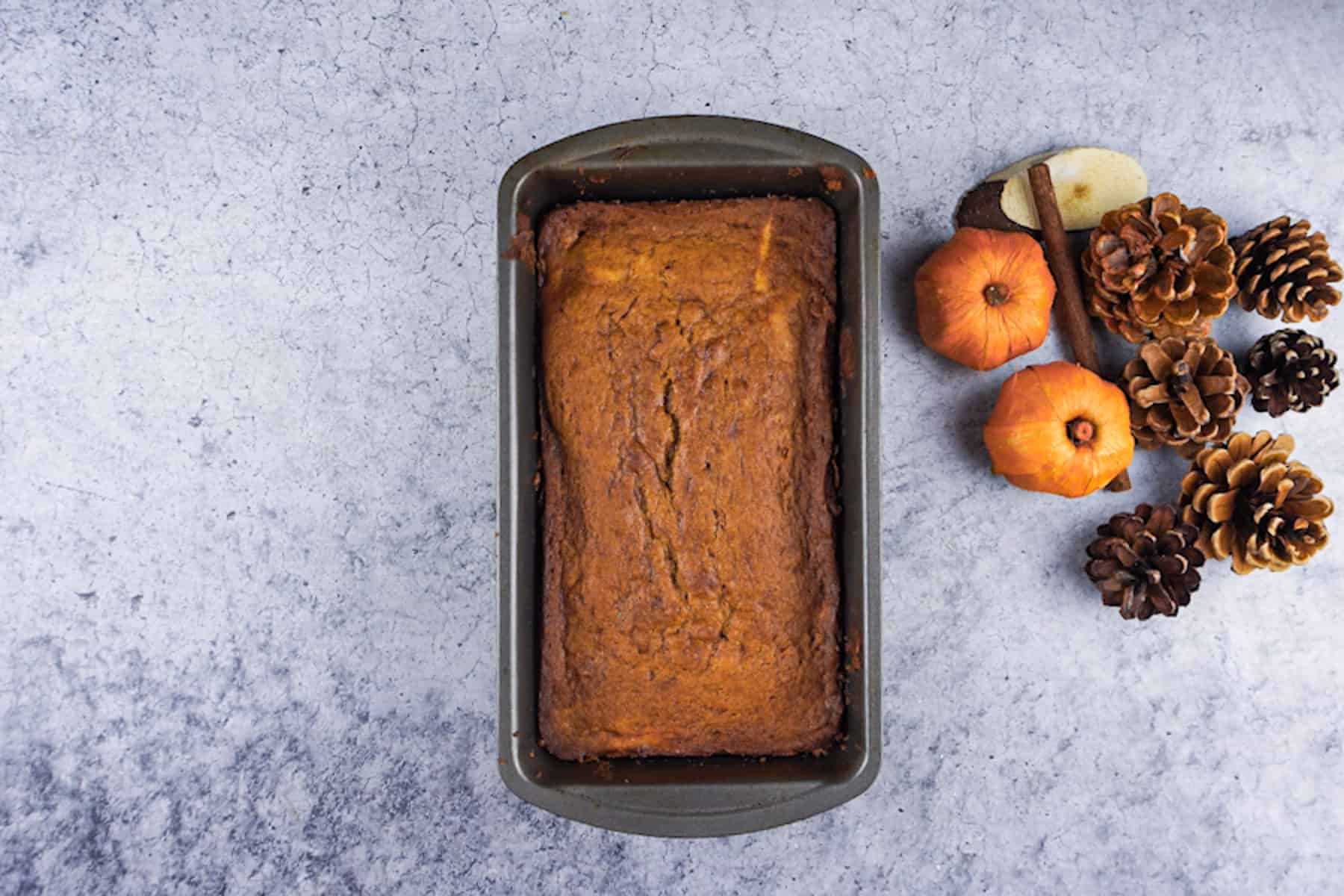 Pumpkin bread baked in a loaf pan next to fall decorations.