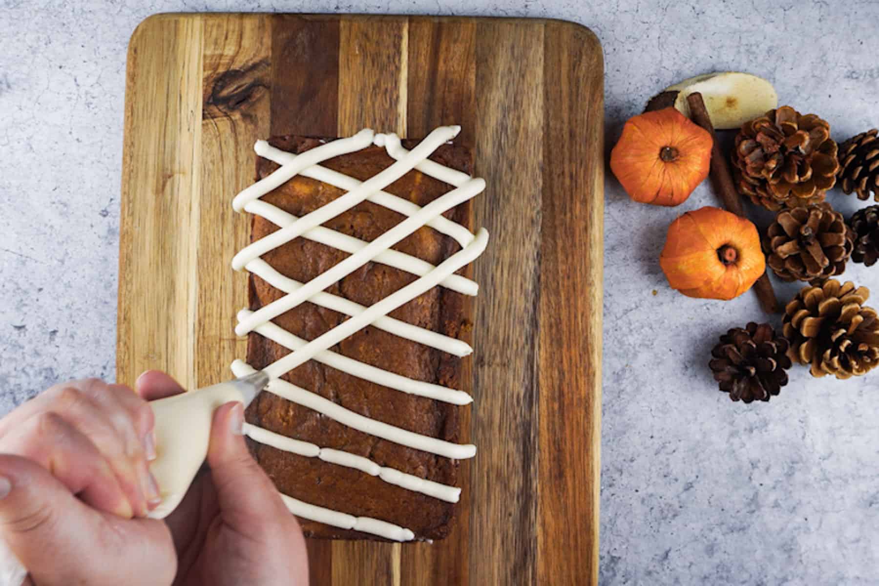 Frosting the pumpkin bread with cream cheese frosting in a crisscross pattern