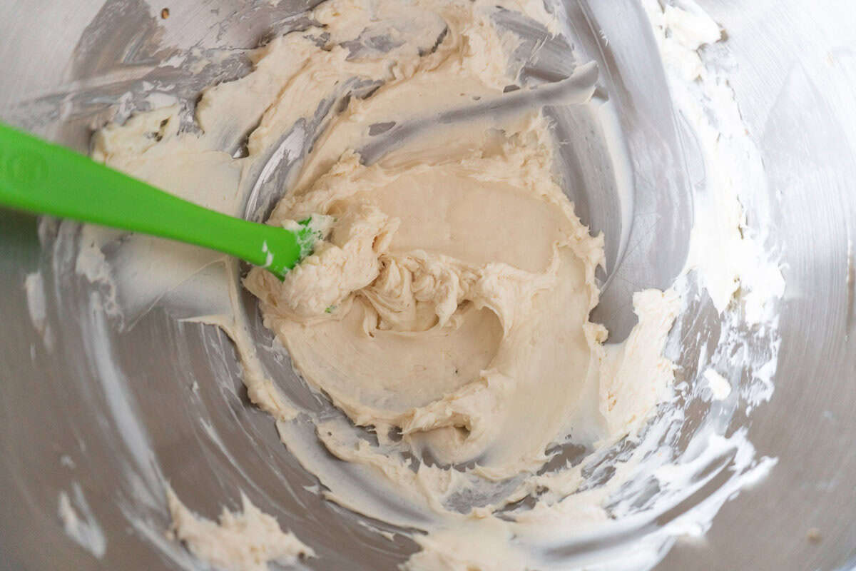 mixed butter and cream cheese in metal mixing bowl with green rubber spatula.
