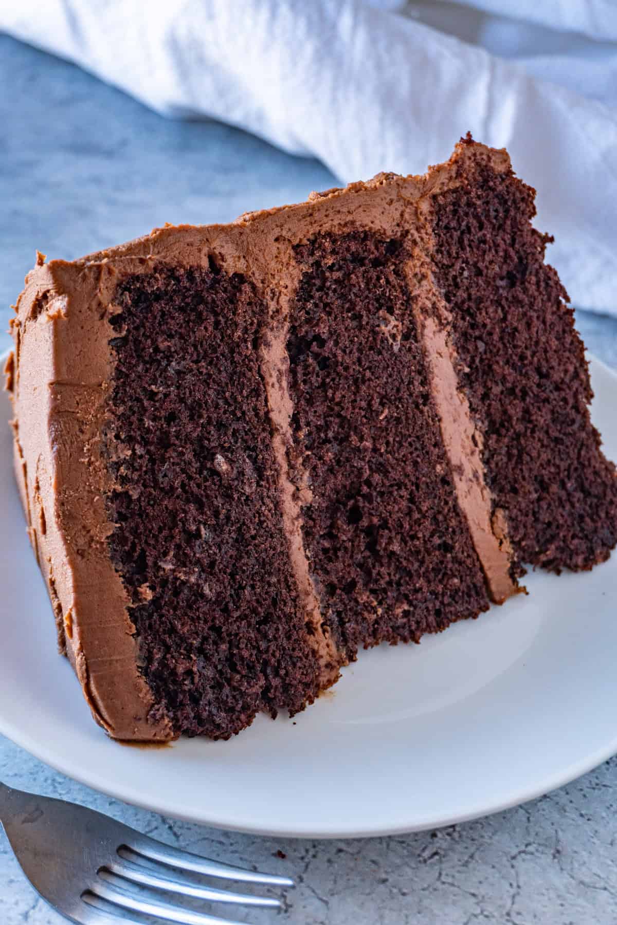 frosted chocolate cake slice with 3 layers on a white plate.
