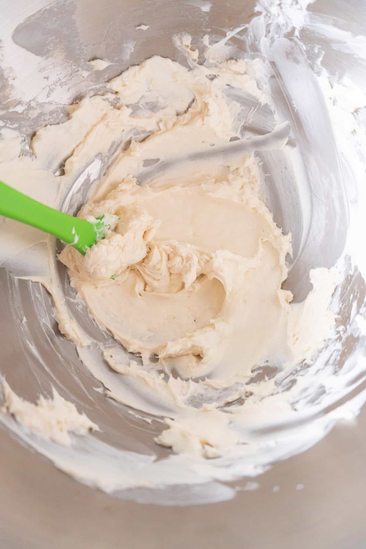 mixed butter and cream cheese in metal mixing bowl with green rubber spatula.