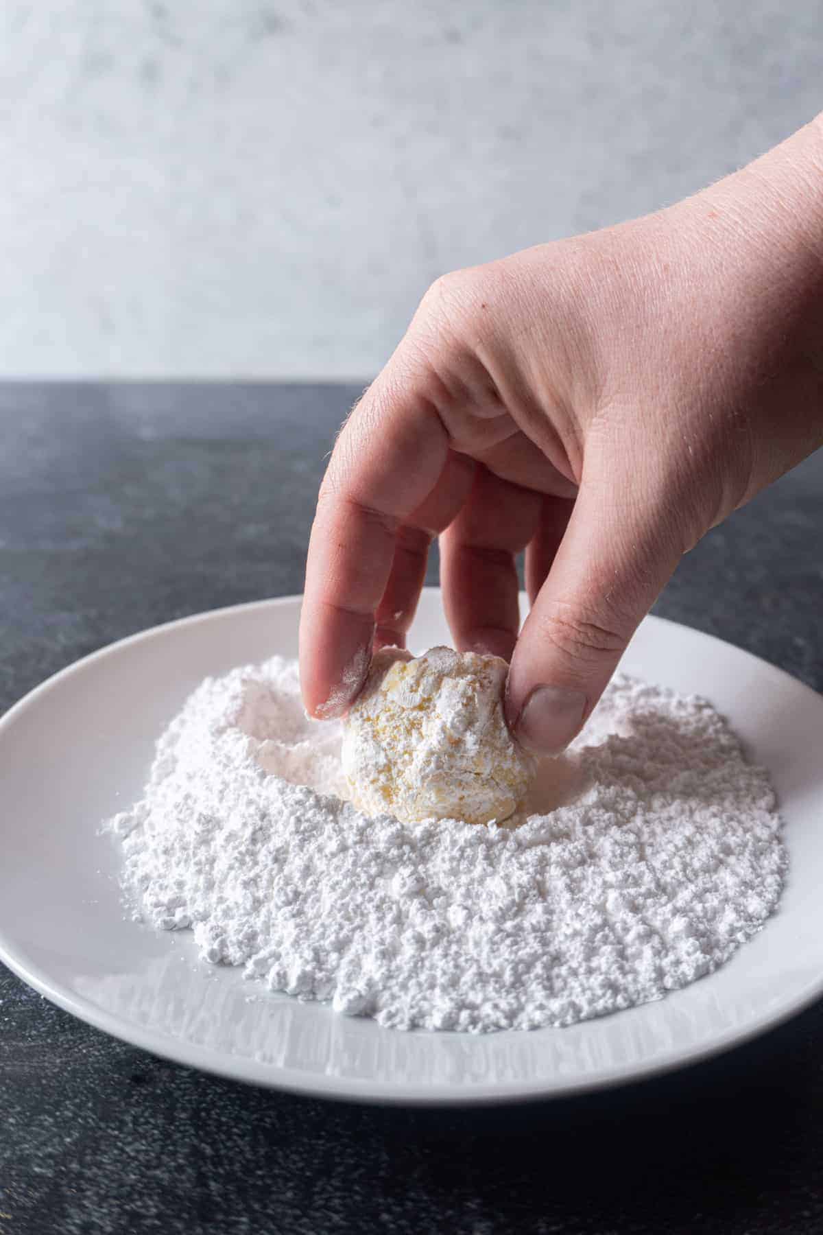 Cookie dough being rolled in powdered sugar