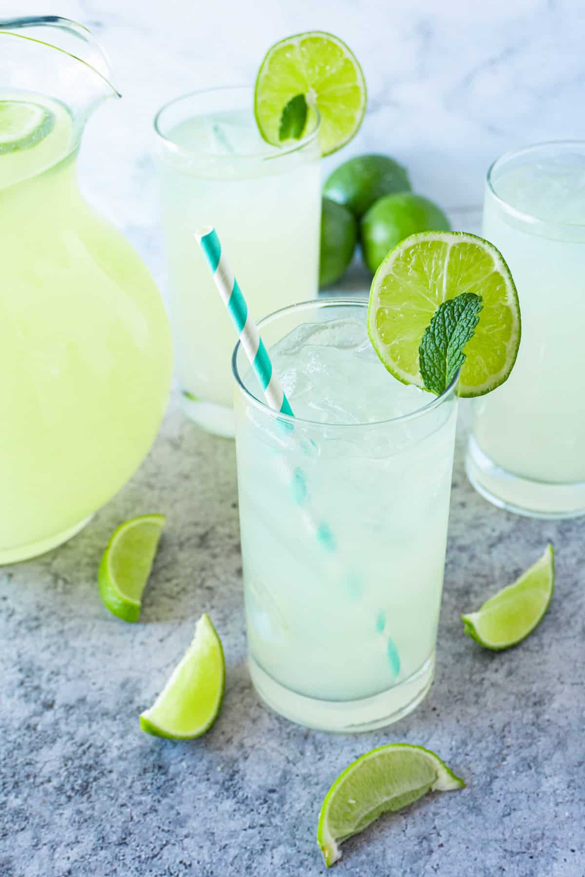 glass filled with limeade, lime wedges lying around it, glass has straw sticking out of it.