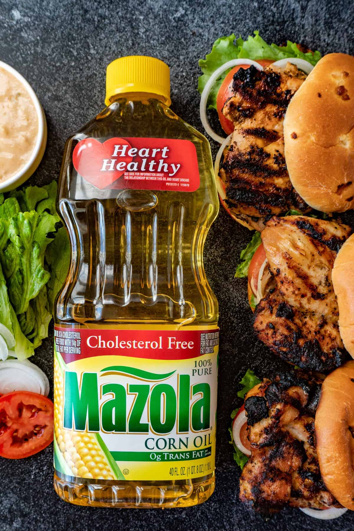 Bottle of Mazola Corn Oil with open faced sandwiches and on one side and condiments on the other