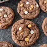chocolate pudding cookies with butterscotch and white chocolate chips laid out on dark background.