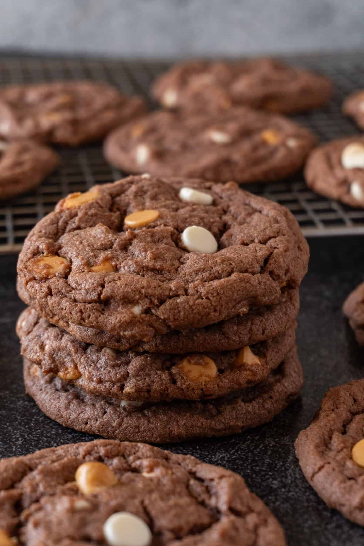 chocolate pudding cookies with butterscotch and white chocolate chips stacked four high, surrounded by more cookies.