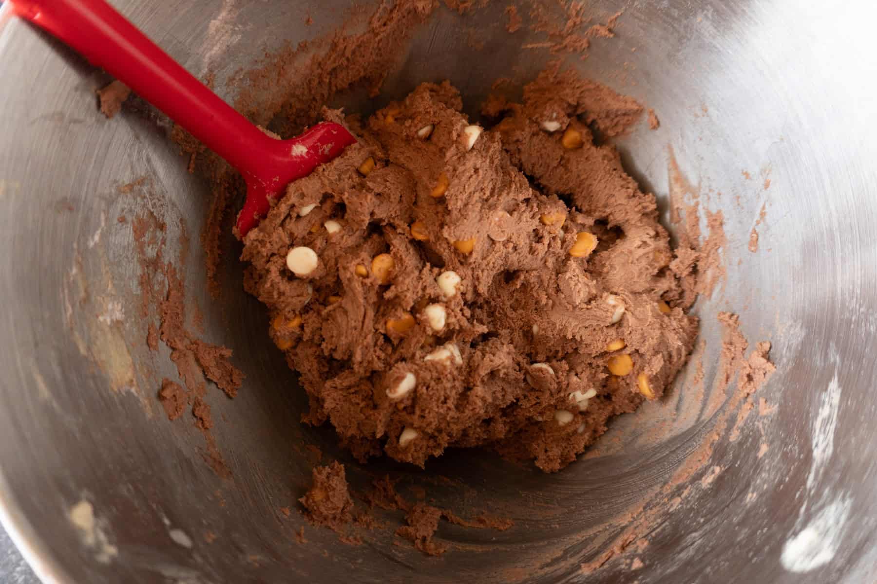 chocolate pudding cookie dough in metal bowl with red spatula.