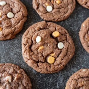 chocolate pudding cookies with butterscotch and white chocolate chips laid out on dark background.