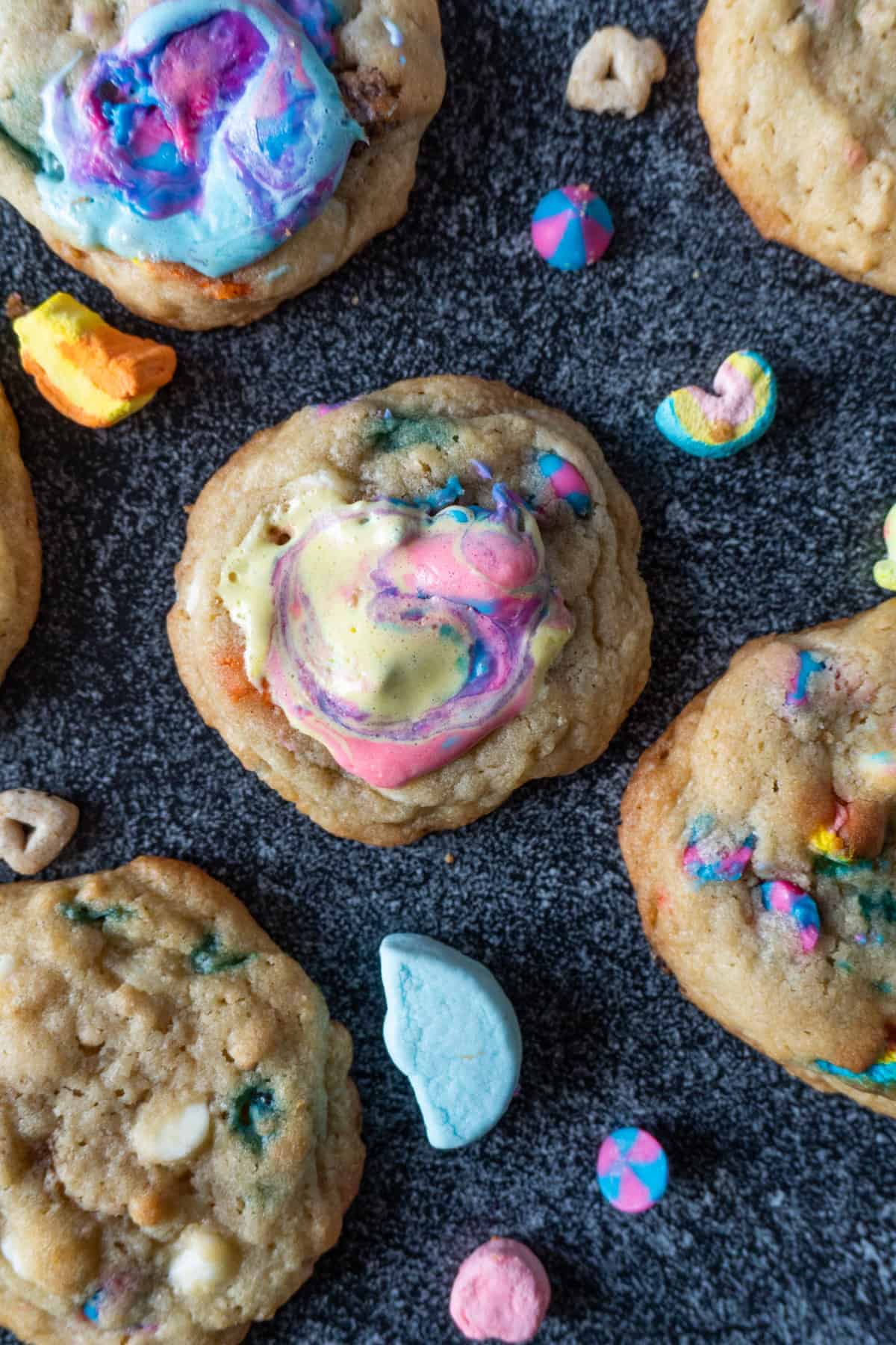 Lucky Charms Cookies are everything magical and super delicious! Filled with cereal bits, crunchy marshmallows, baked to perfection, and topped with gooey marshmallow! #atablefullofjoy #bakery #cookie #chewy #marshmallow #bestcookie #forkids #luckycharms #cereal #rainbow #tiedye #rainbow Lucky Charms Cookies with lucky charms cereal around it