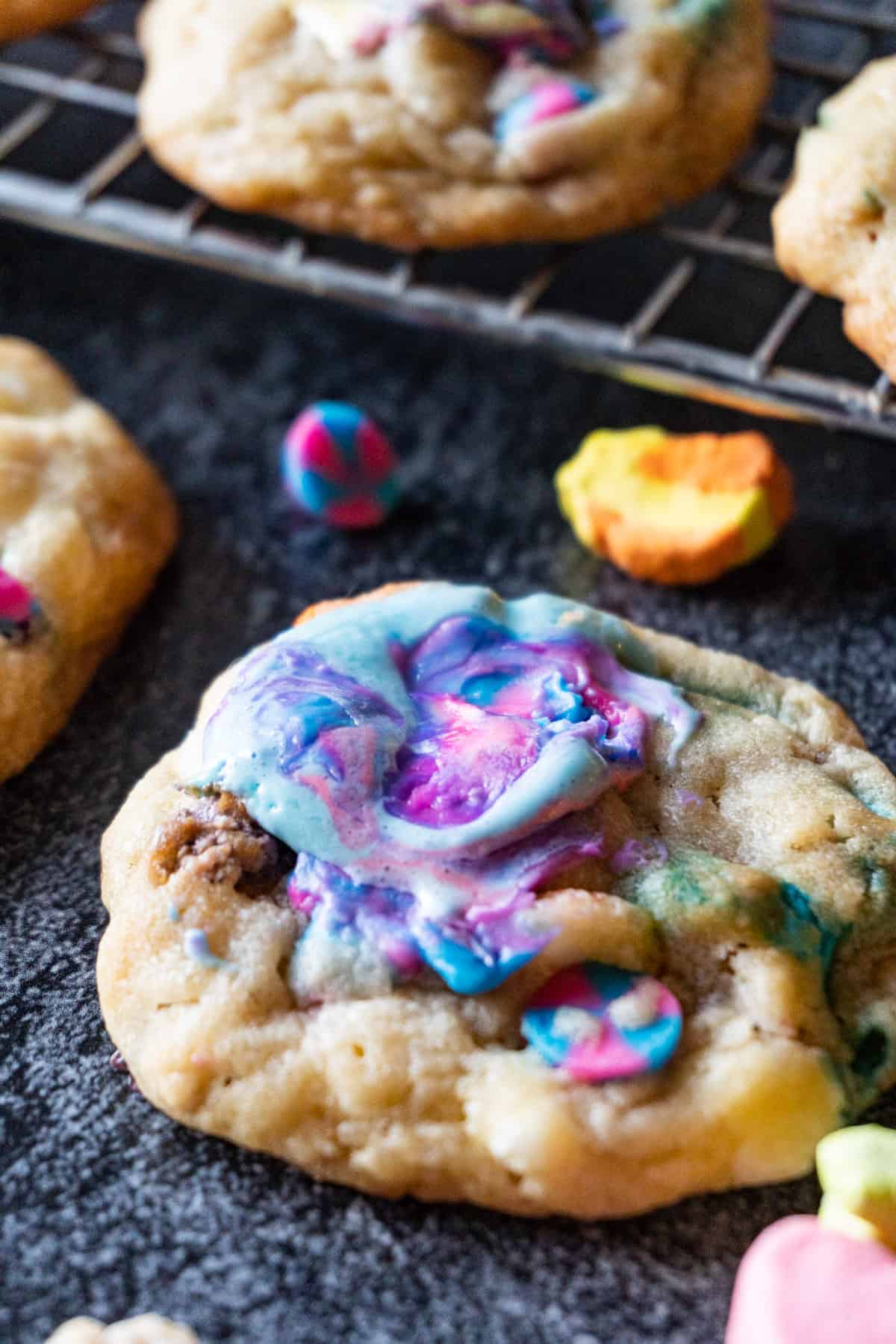 Lucky Charms Cookies are everything magical and super delicious! Filled with cereal bits, crunchy marshmallows, baked to perfection, and topped with gooey marshmallow! #atablefullofjoy #bakery #cookie #chewy #marshmallow #bestcookie #forkids #luckycharms #cereal #rainbow #tiedye #rainbow Lucky Charms Cookies with purple marshmallow melted on top