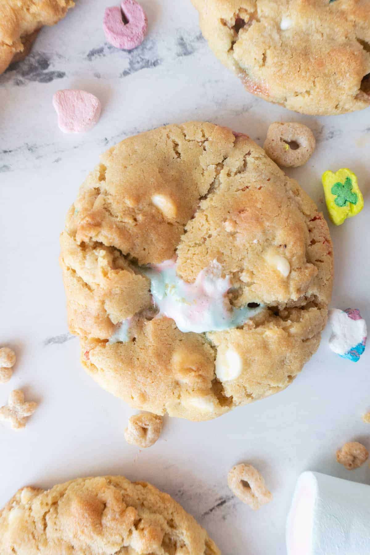 Lucky Charms Cookies are everything magical and super delicious! Filled with cereal bits, crunchy marshmallows, baked to perfection, and topped with gooey marshmallow! #atablefullofjoy #bakery #cookie #chewy #marshmallow #bestcookie #forkids #luckycharms #cereal #rainbow #tiedye #rainbow Lucky Charms Cookie Close Up with marshmallow coming out