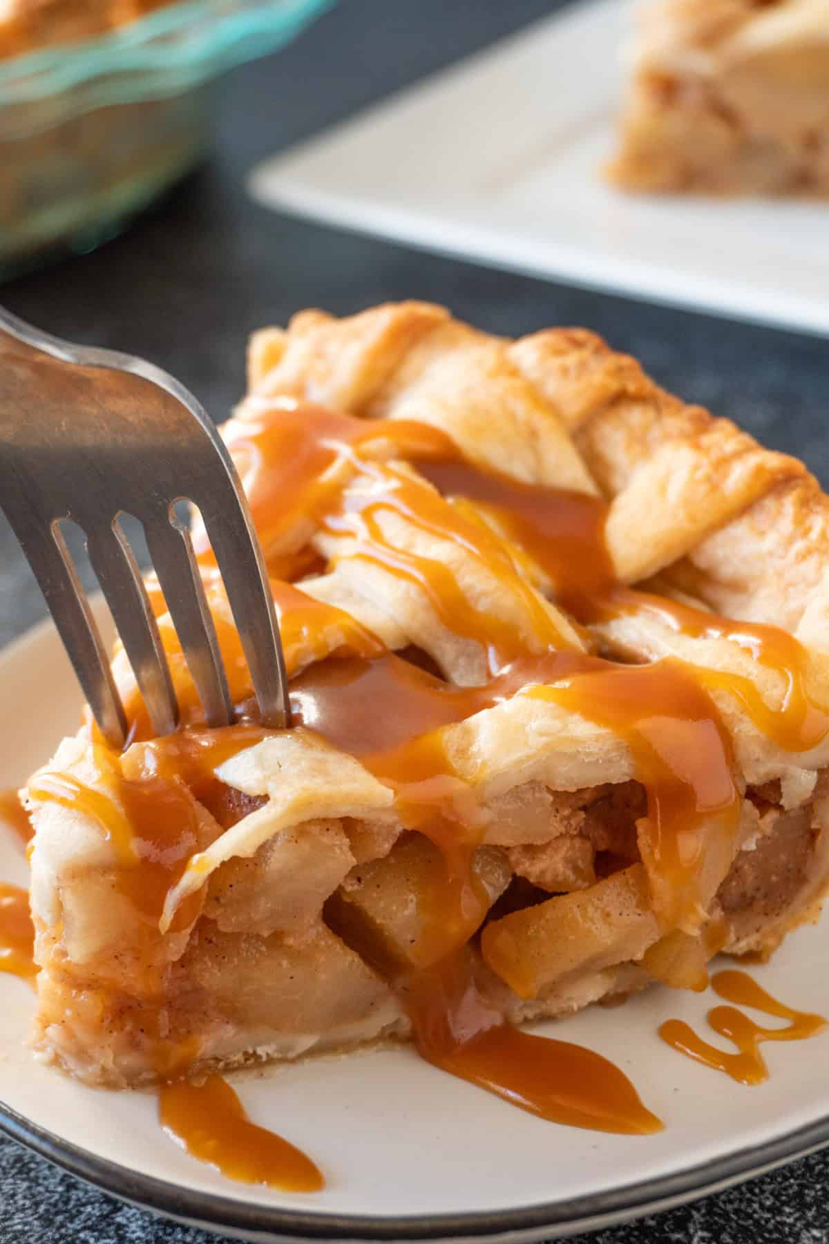 Sticking a fork into a slice of caramel pear pie on a white round plate.
