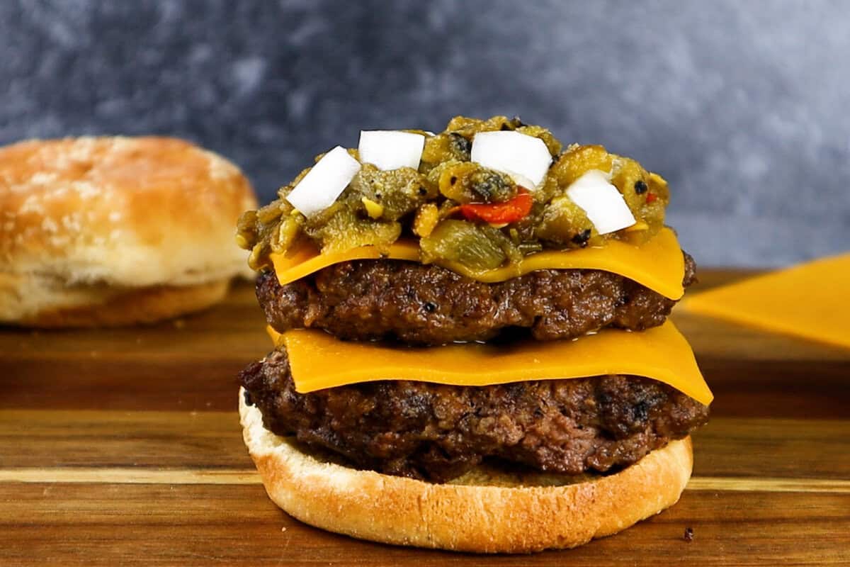 green chile cheeseburger being assembled- 2 patties with cheese. green chile and onion. 