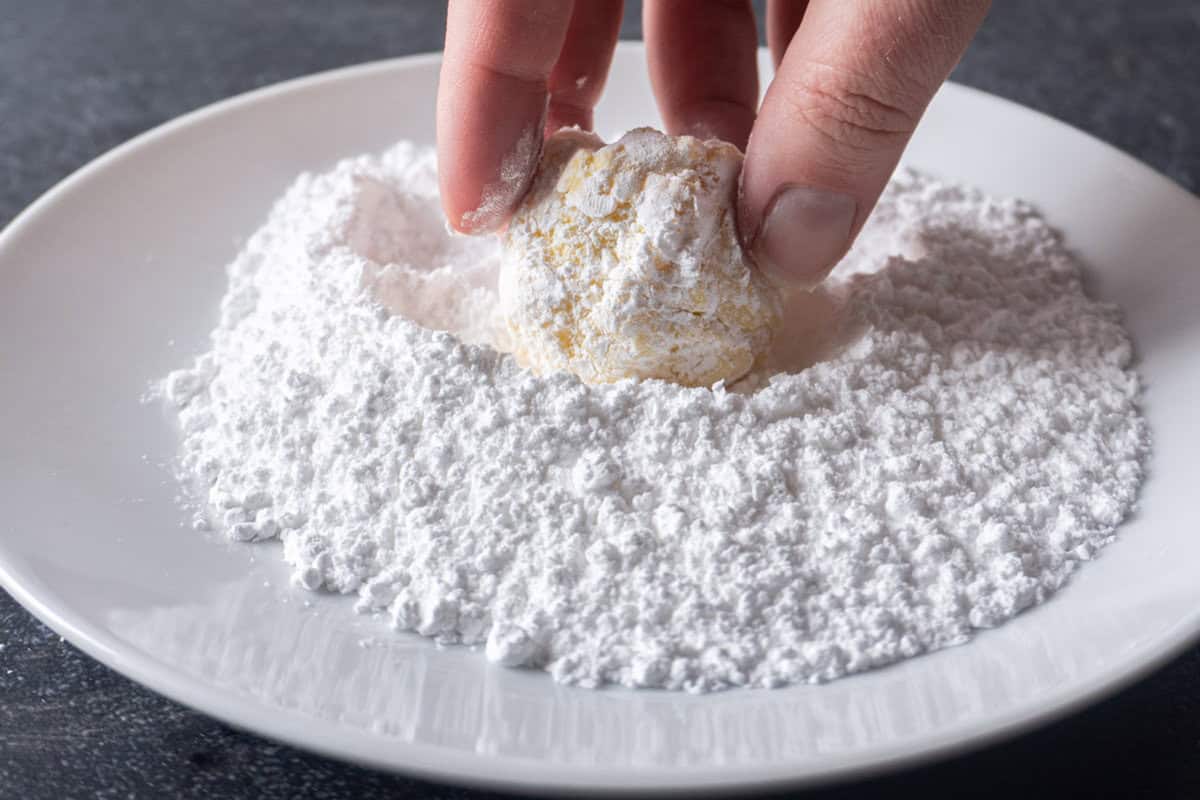 rolling lemon cake cookie dough in powdered sugar.