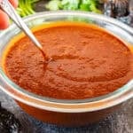 stirring red enchilada sauce with metal spoon.