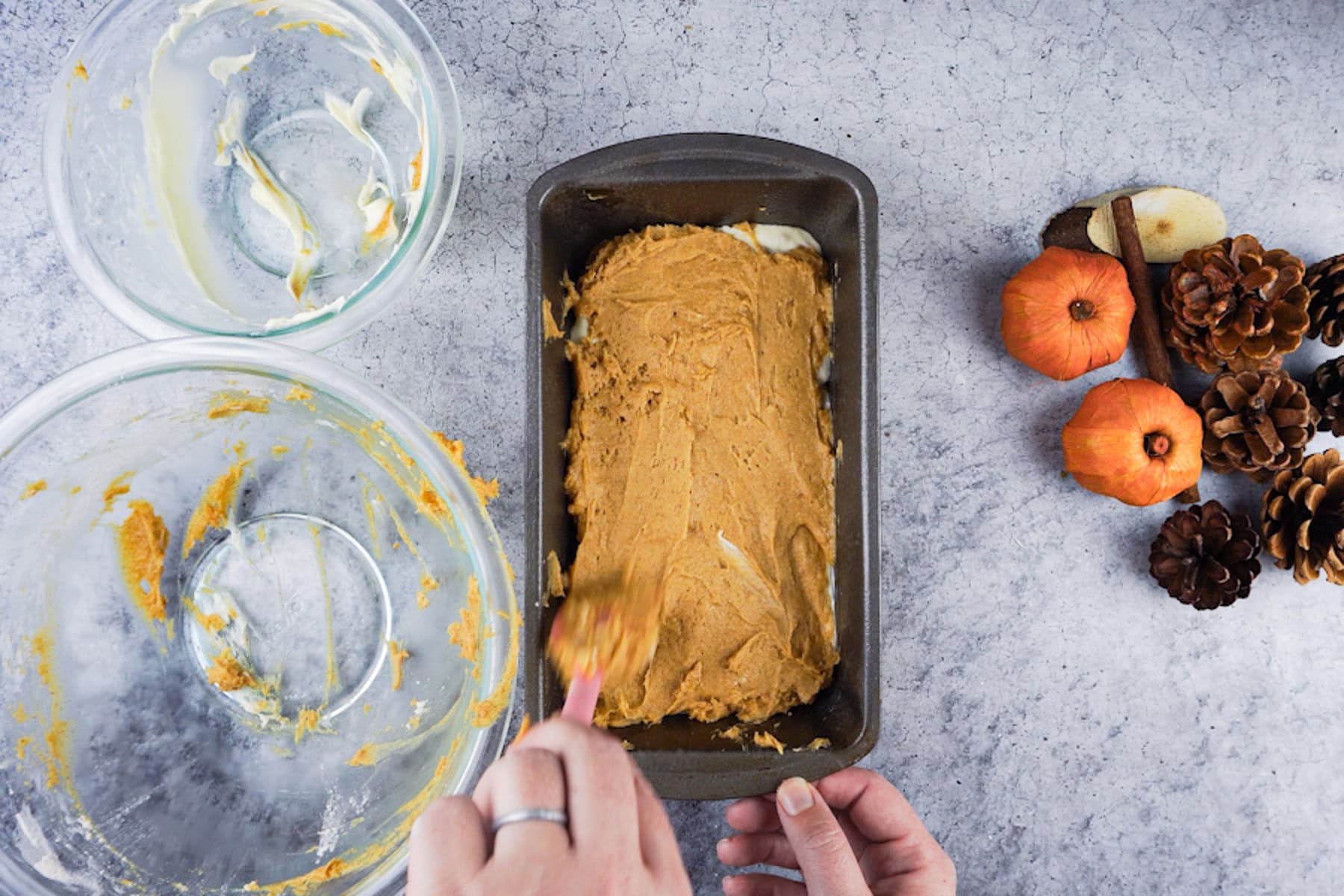 Spreading pumpkin bread batter over the cream cheese filling layer in a loaf pan.