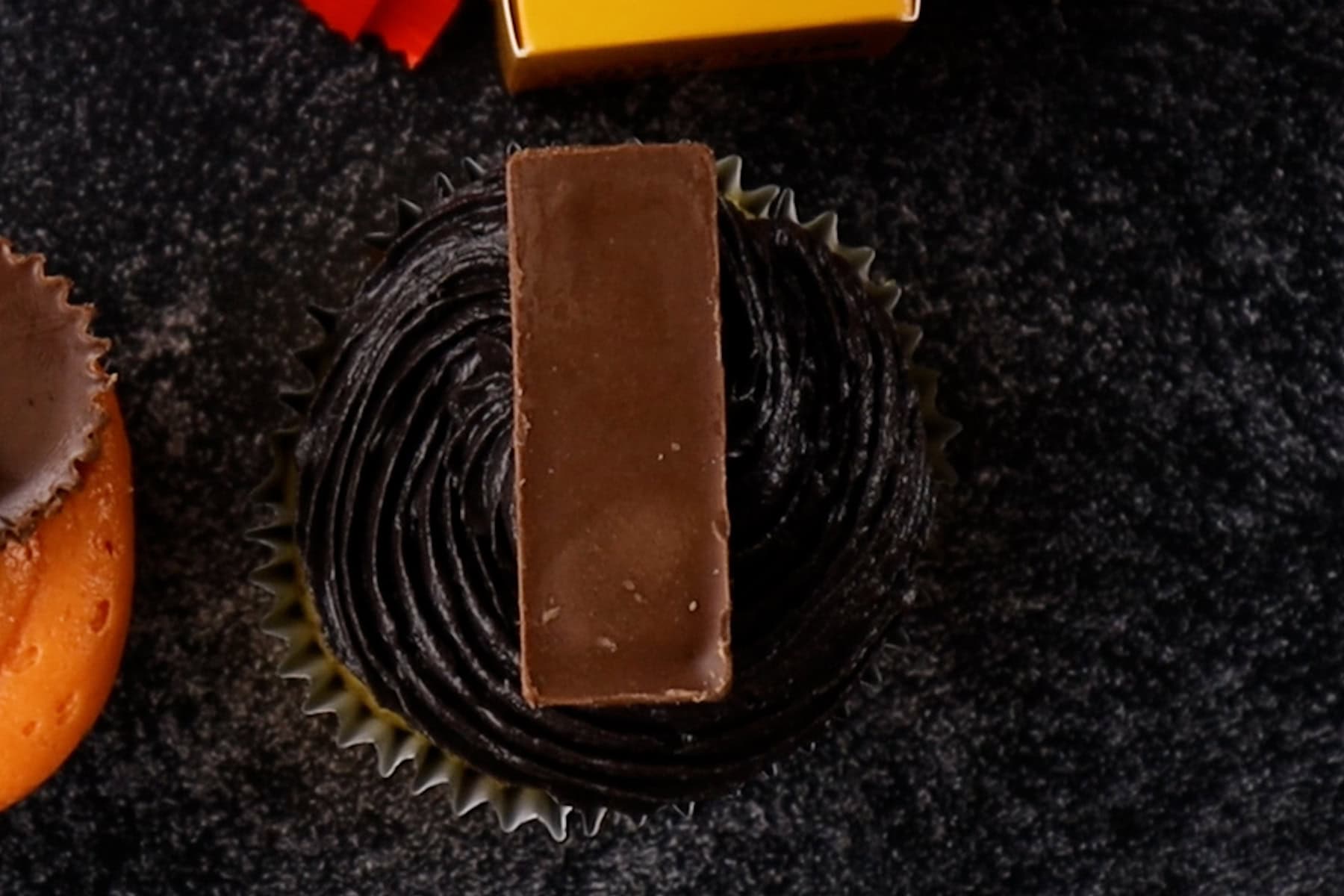 KitKat Miniature placed upside down on a black frosted cupcake.