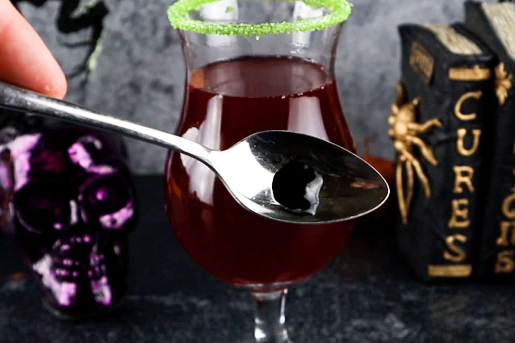 pea sized amount of black food gel on a spoon in front of a cocktail being made.