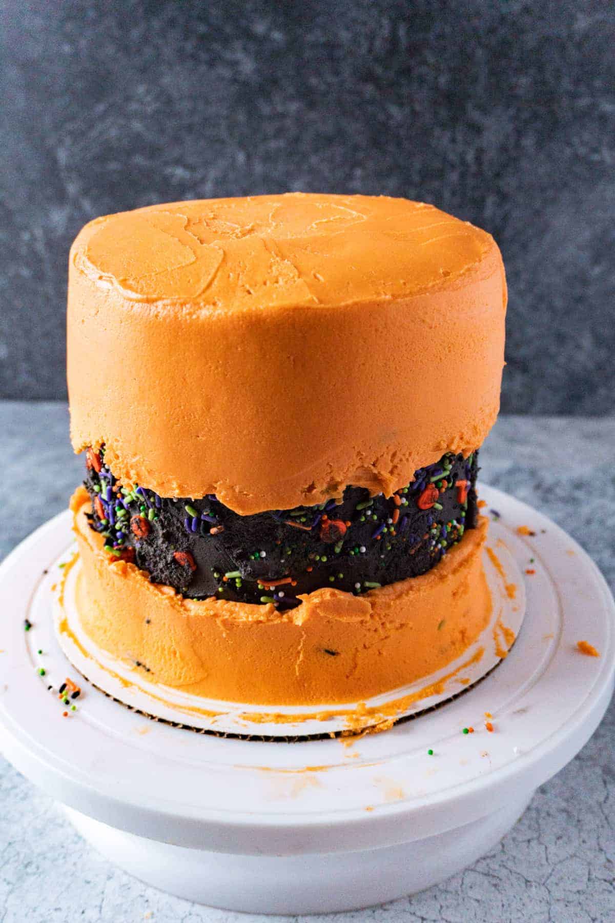 Cake with a final coat of orange buttercream on the top and bottom, leaving the black band in the center to show through.