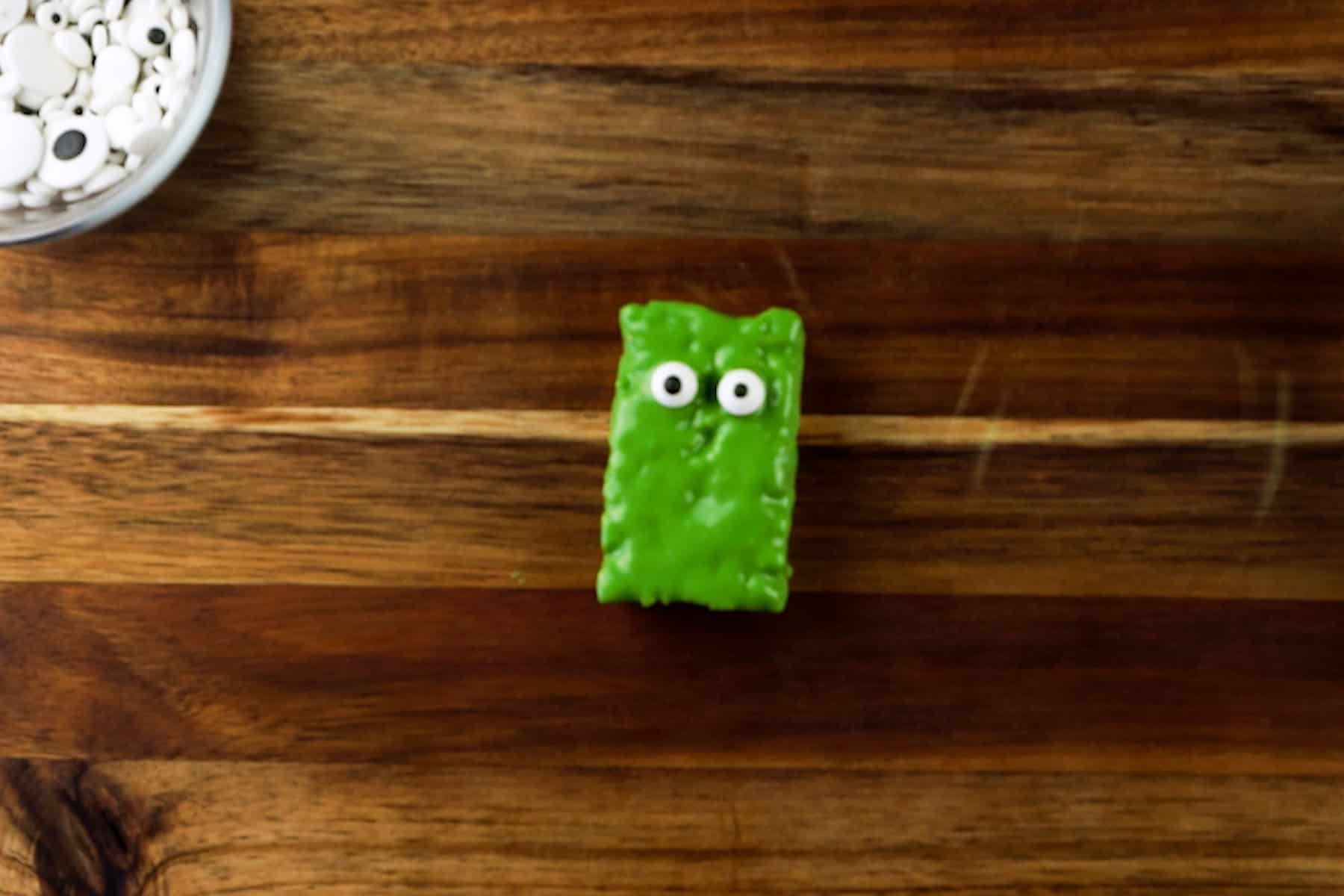 rice krispy rectangle dipped in green candy melts with candy eyes pressed on.