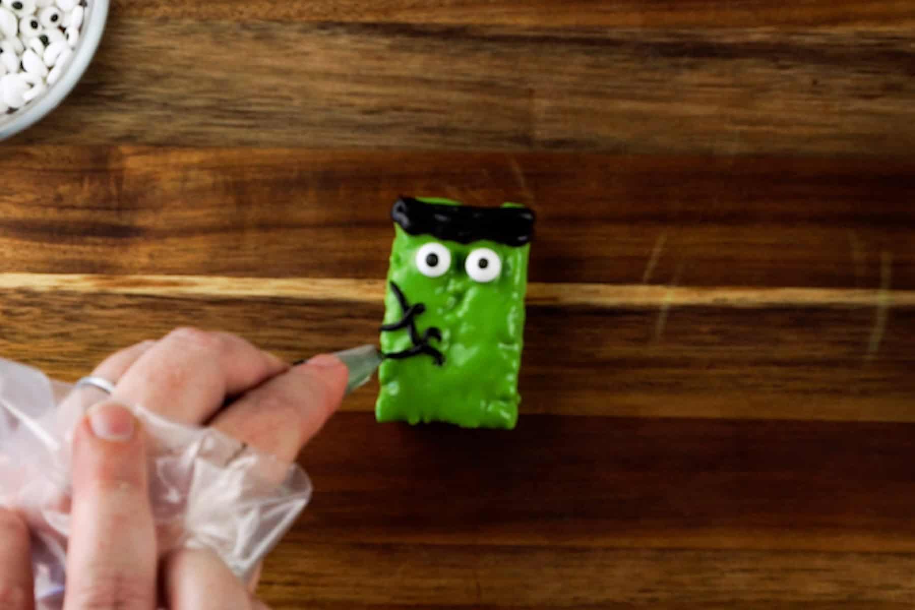 rice krispy rectangle dipped in green candy melts, decorated to look like Frankenstein's monster..