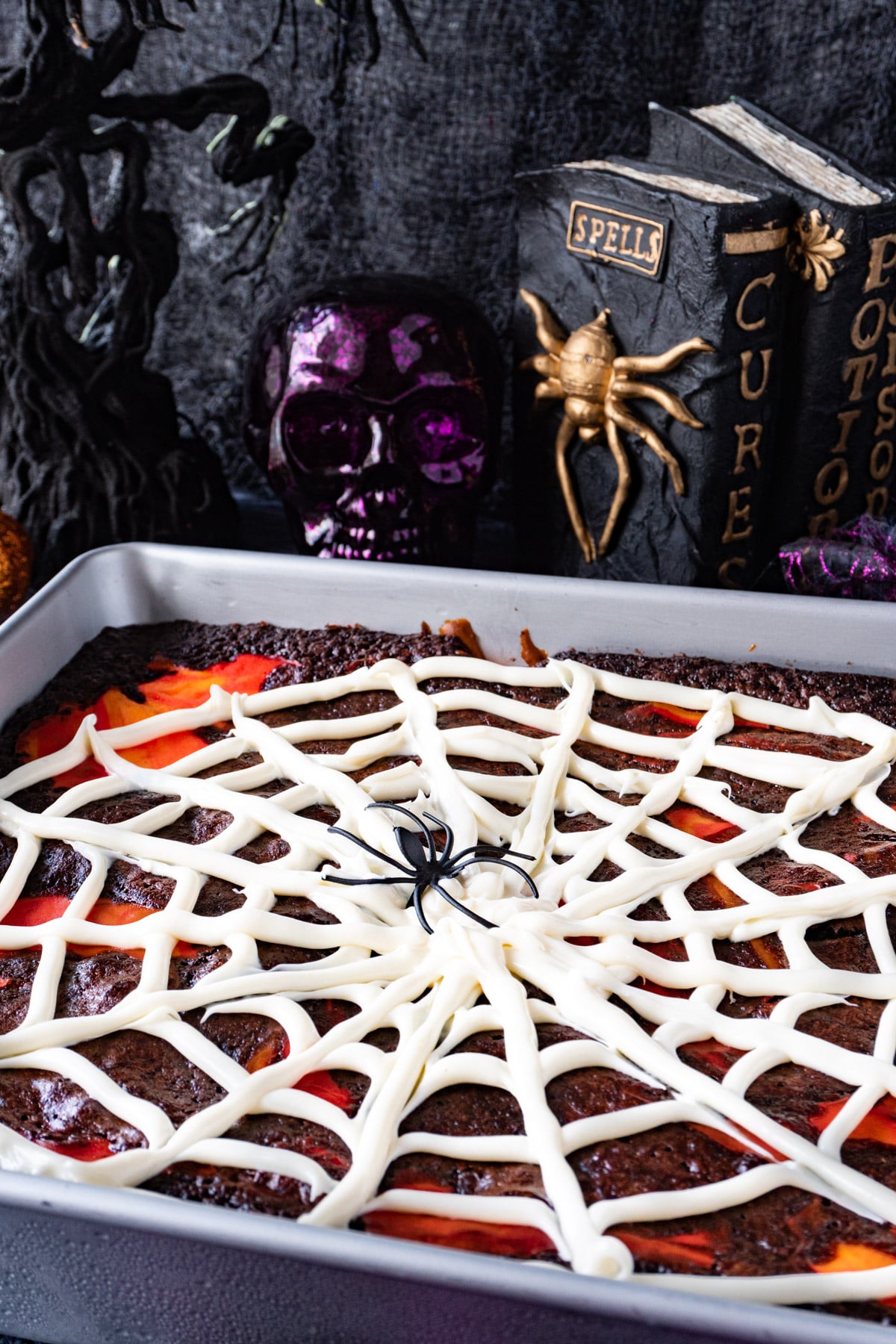 Spiderweb brownies in a pan with Halloween decorations in the background.