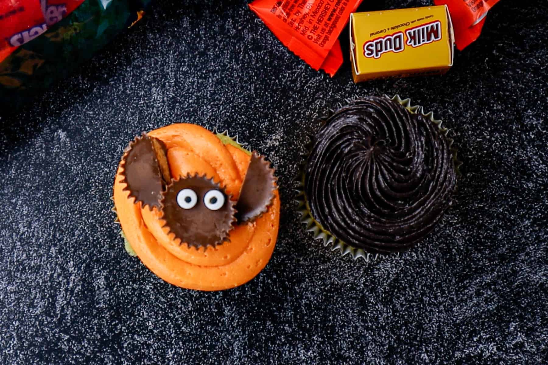 Orange and black frosted cupcakes. The orange cupcake features a bat made from mini Reese's on top.