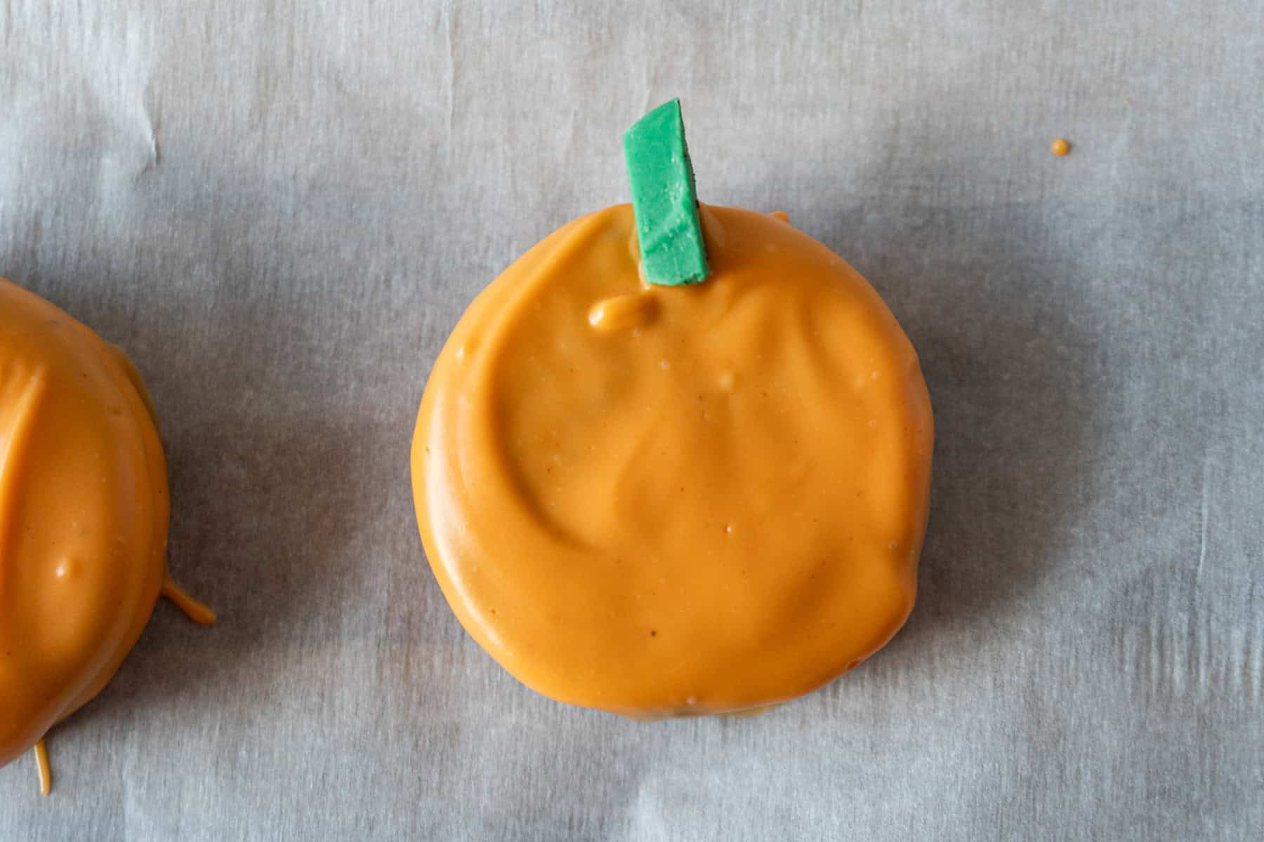Oreo dipped in orange candy melts with a sliver of green candy melt pressed on top to be the pumpkin stem.