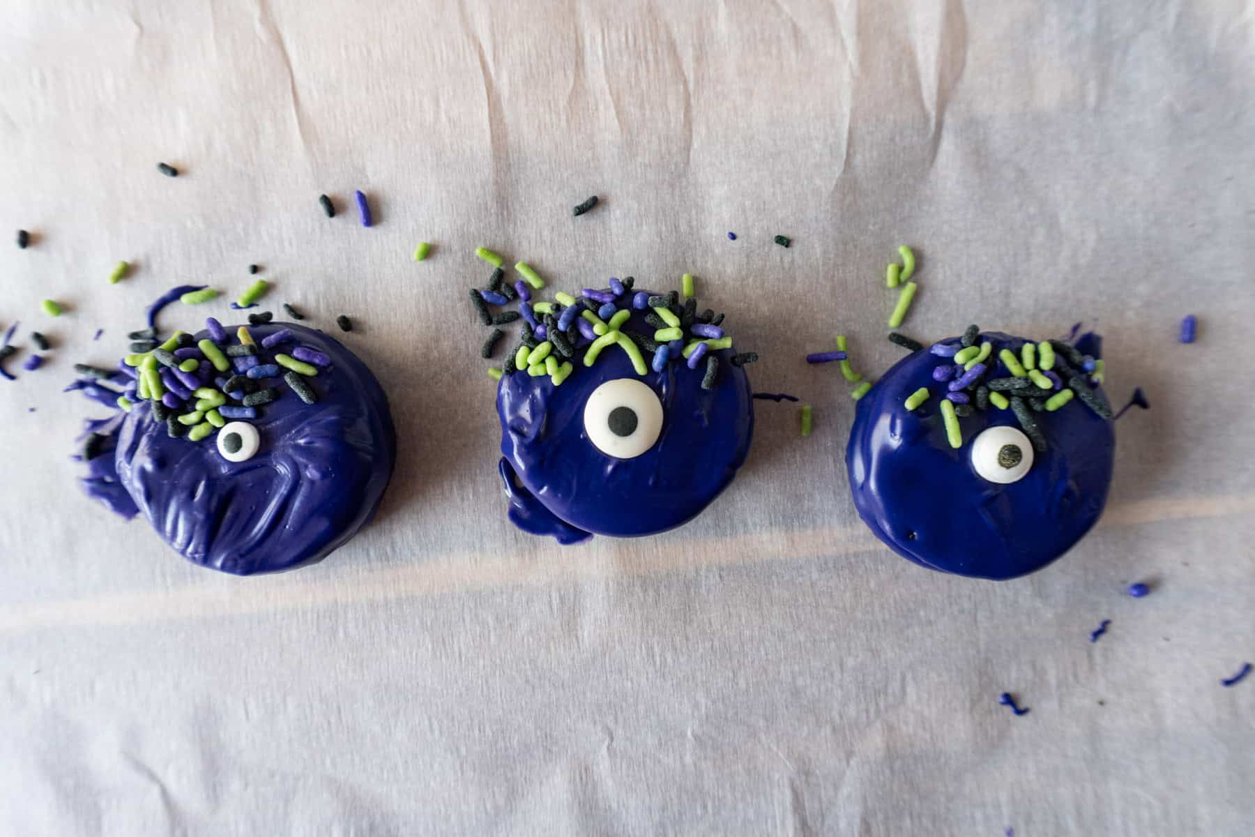 Oreos covered in purple candy melts with a candy eye and sprinkles decorating it.