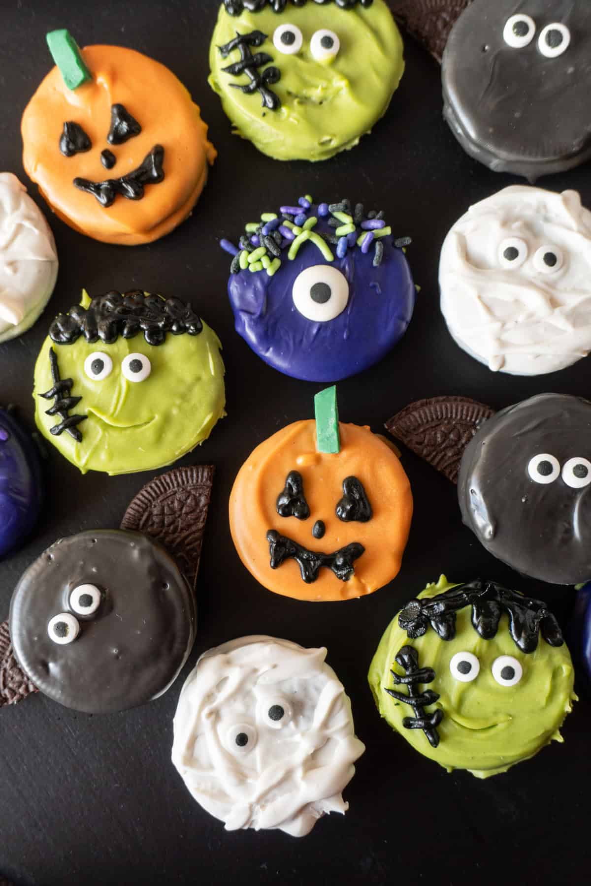 Halloween Oreos all decorated as different Halloween Themes on a black background surrounded by pumpkin lights and purple