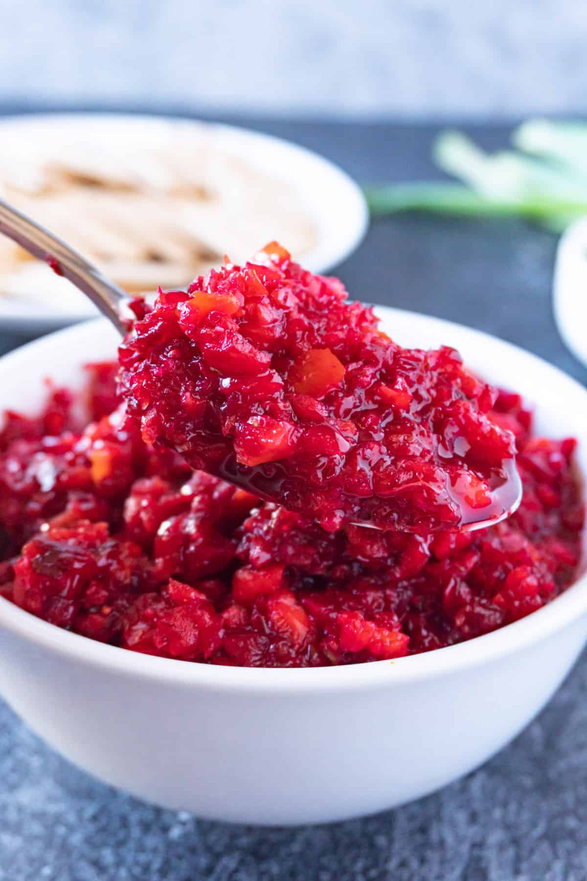 scooping cranberry relish out of a white bowl with a spoon.