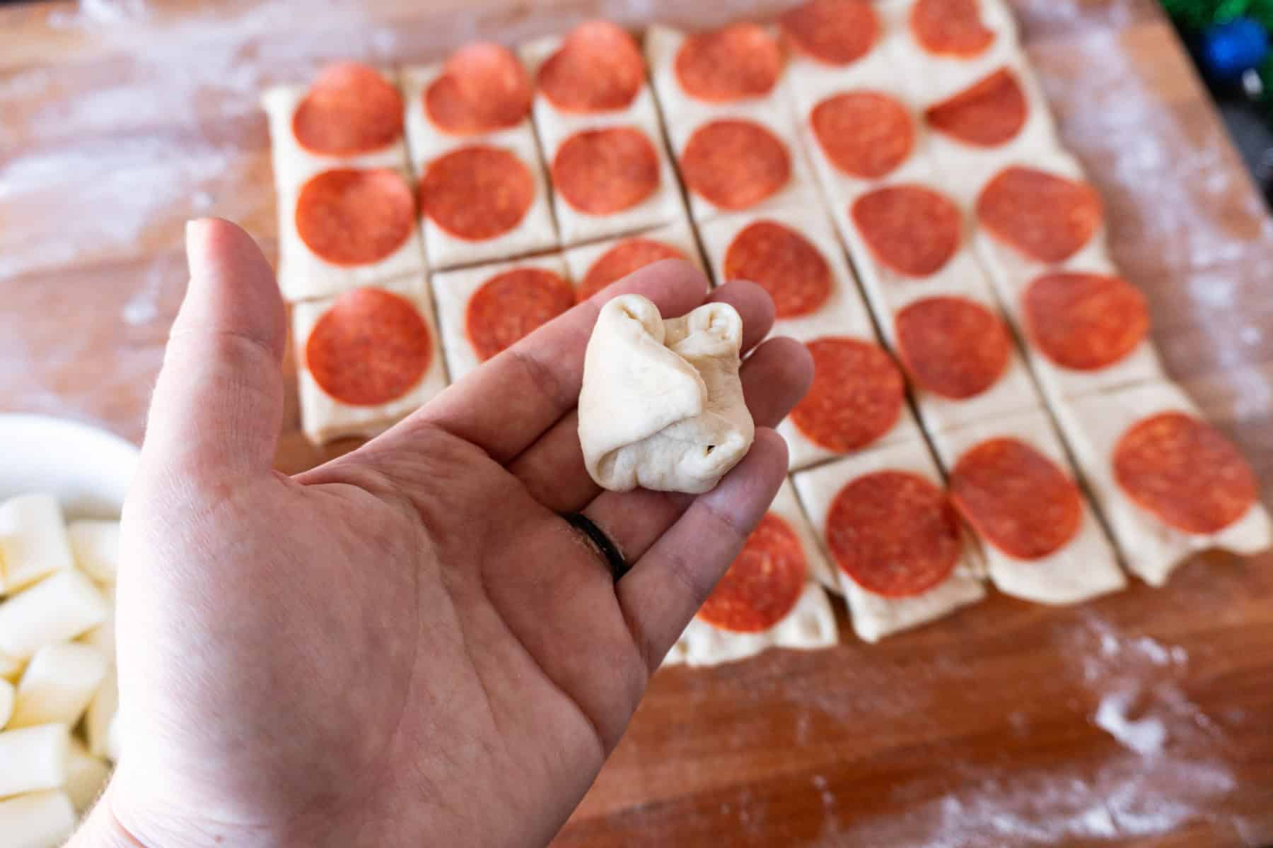 rolling a dough ball with pepperoni and cheese in center.