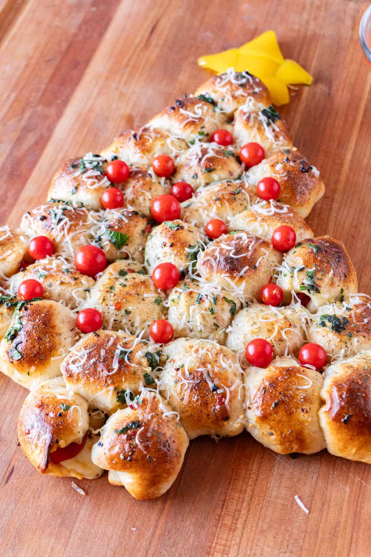 Christmas Tree Appetizer on wooden cutting board shoing details of small tomatoes and green herbs brushed on.