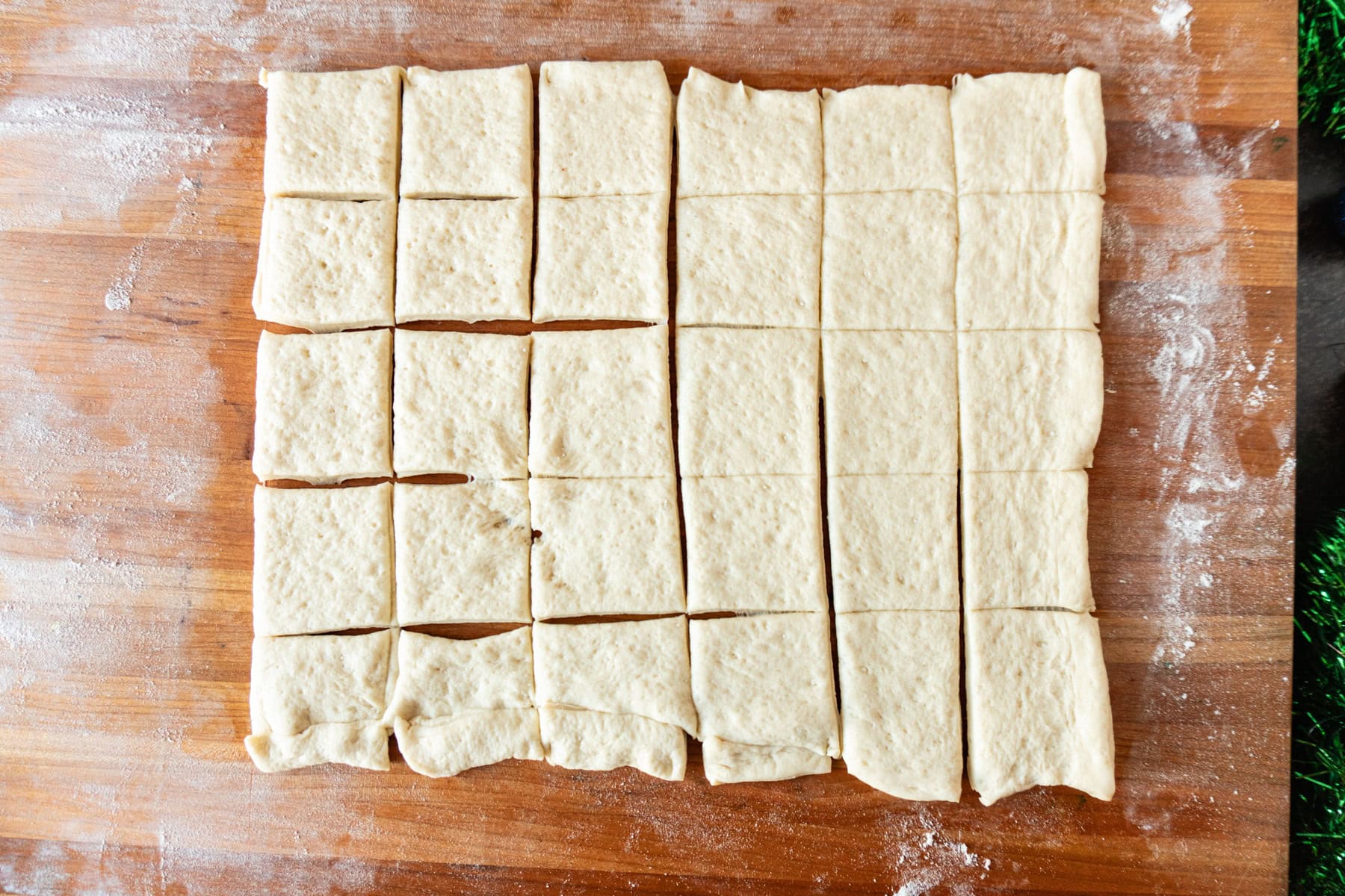 pizza dough rolled out on wooden cutting board and cut into squares.