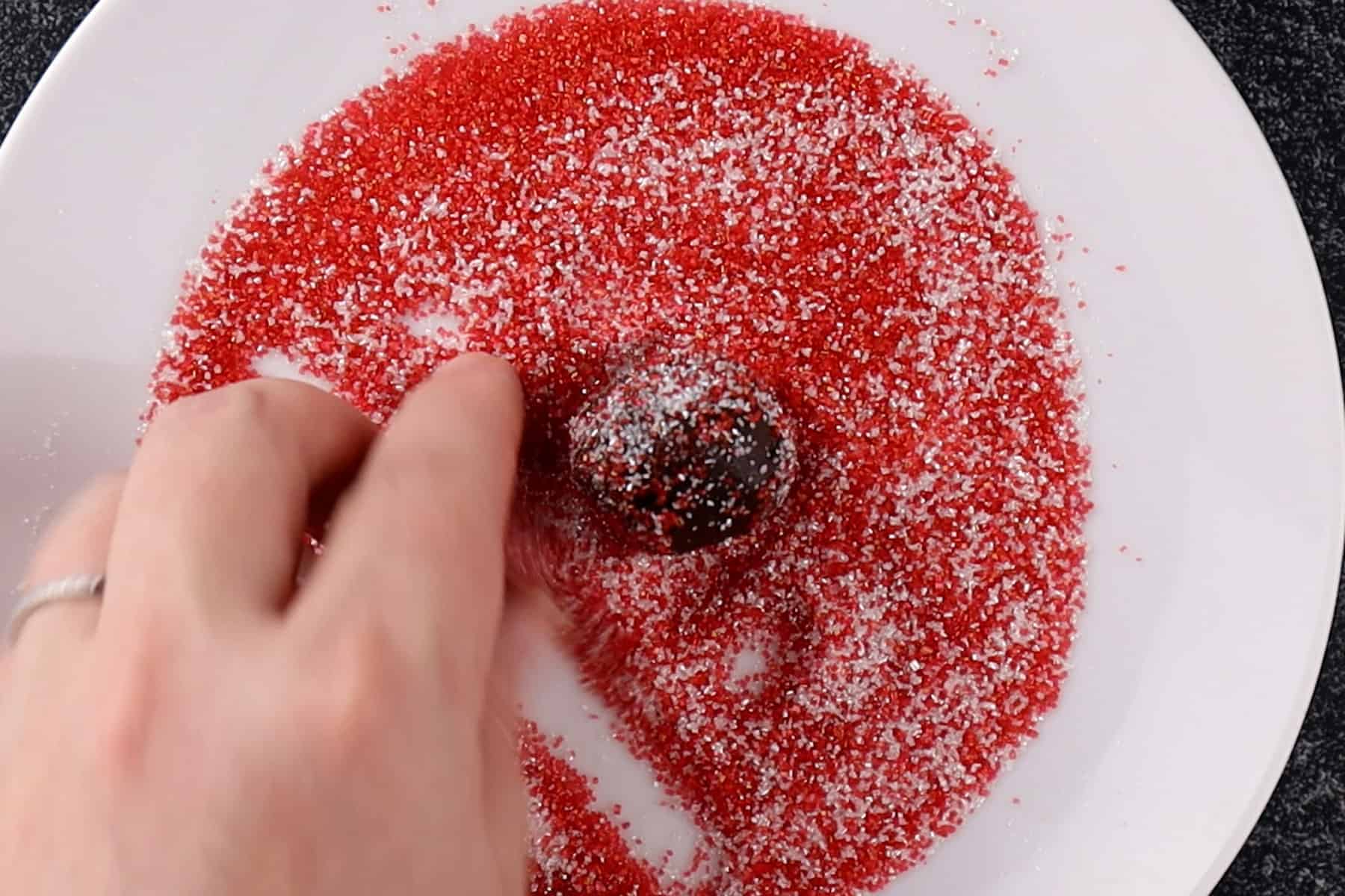 rolling chocolate truffle in red sprinkles on a white plate.